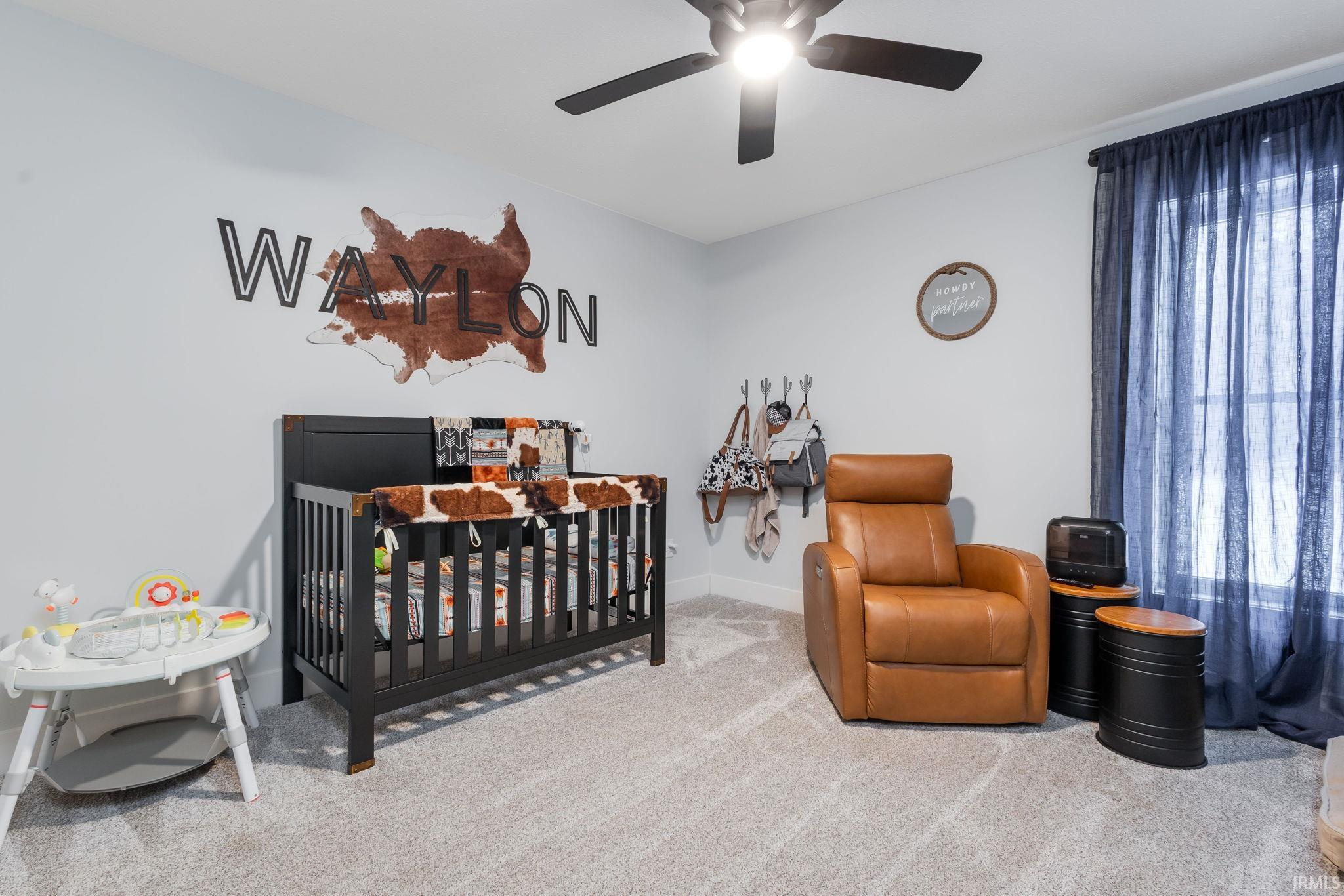 Carpeted bedroom featuring a nursery area and ceiling fan
