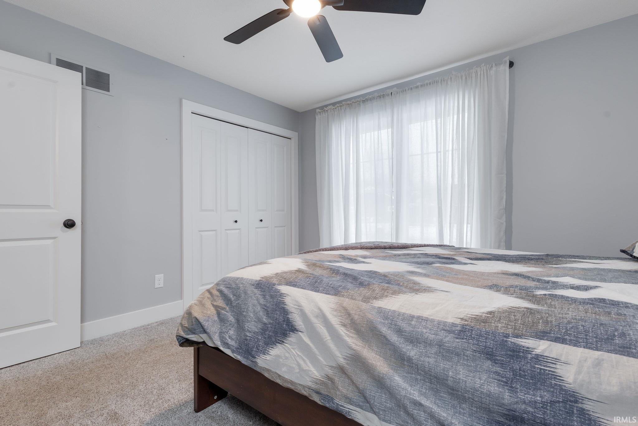 Bedroom featuring light colored carpet, a ceiling fan, and a closet