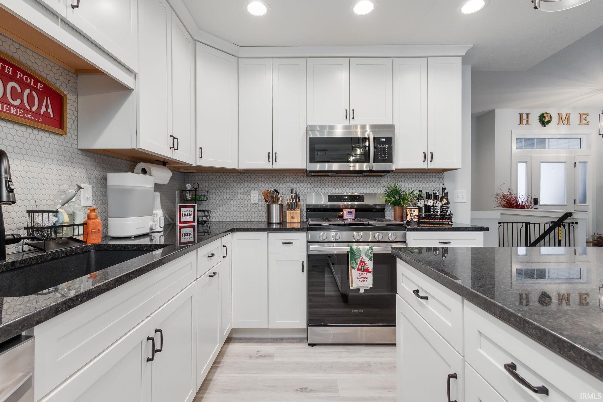 Kitchen featuring appliances with stainless steel finishes, dark stone counters, white cabinets, light wood-type flooring, and recessed lighting