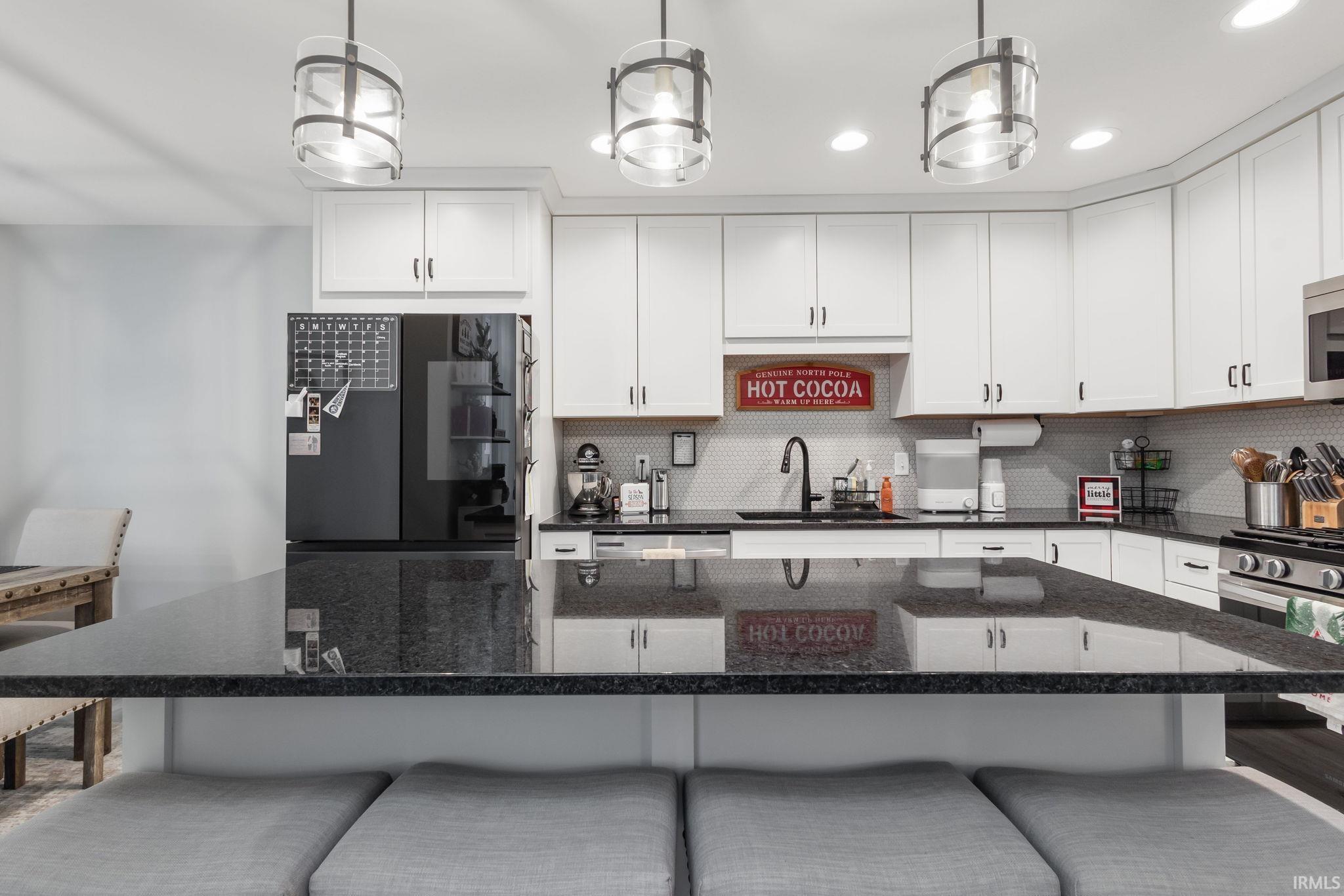 Kitchen with dark stone counters, a breakfast bar, white cabinetry, stainless steel appliances, and recessed lighting