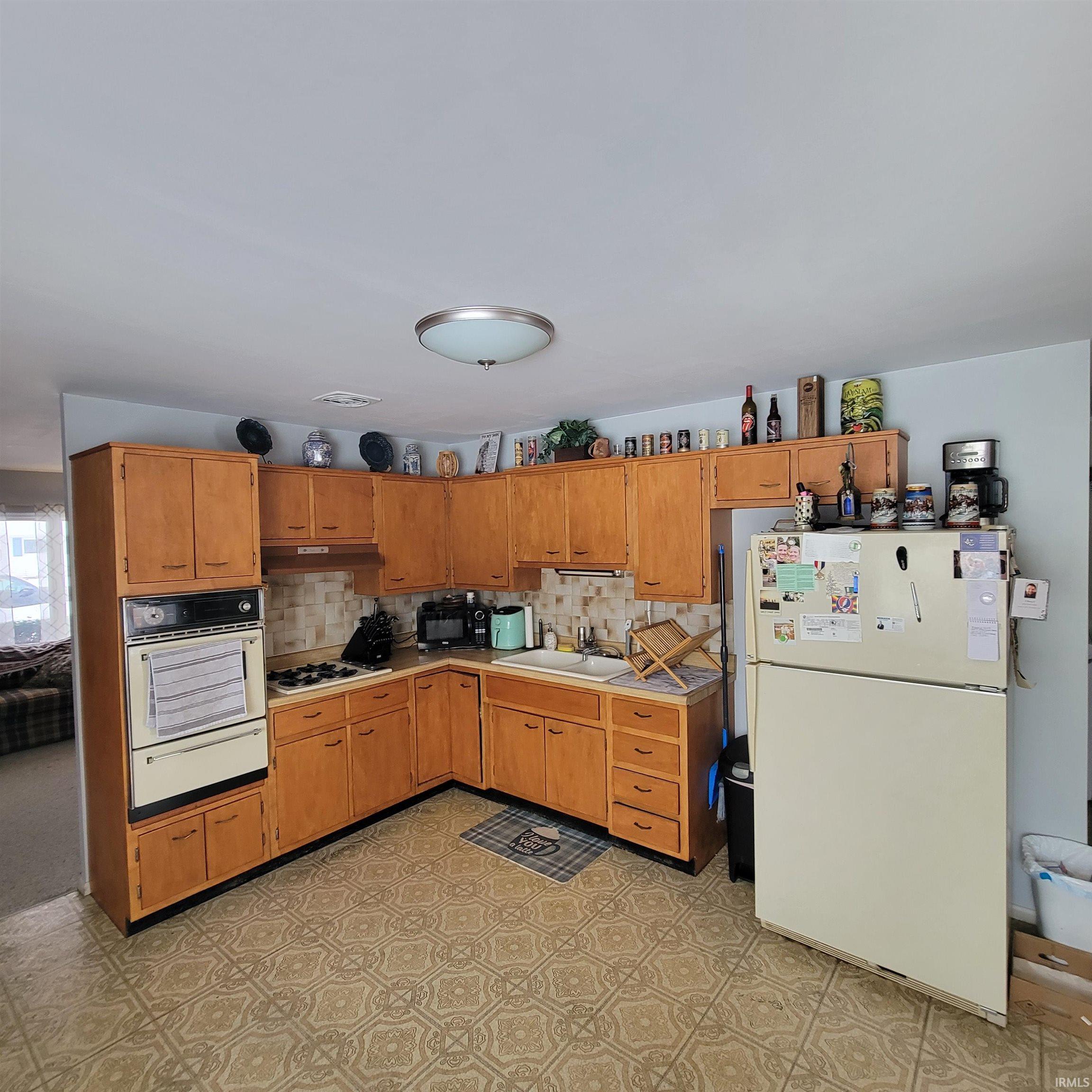 Kitchen with white appliances, light floors, a warming drawer, brown cabinetry, and light countertops