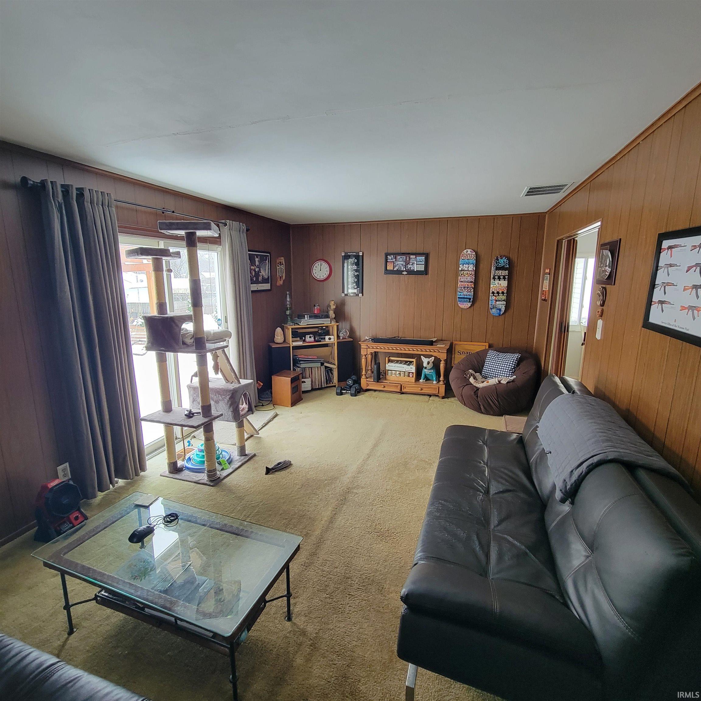 Living area with healthy amount of natural light, wood walls, and carpet