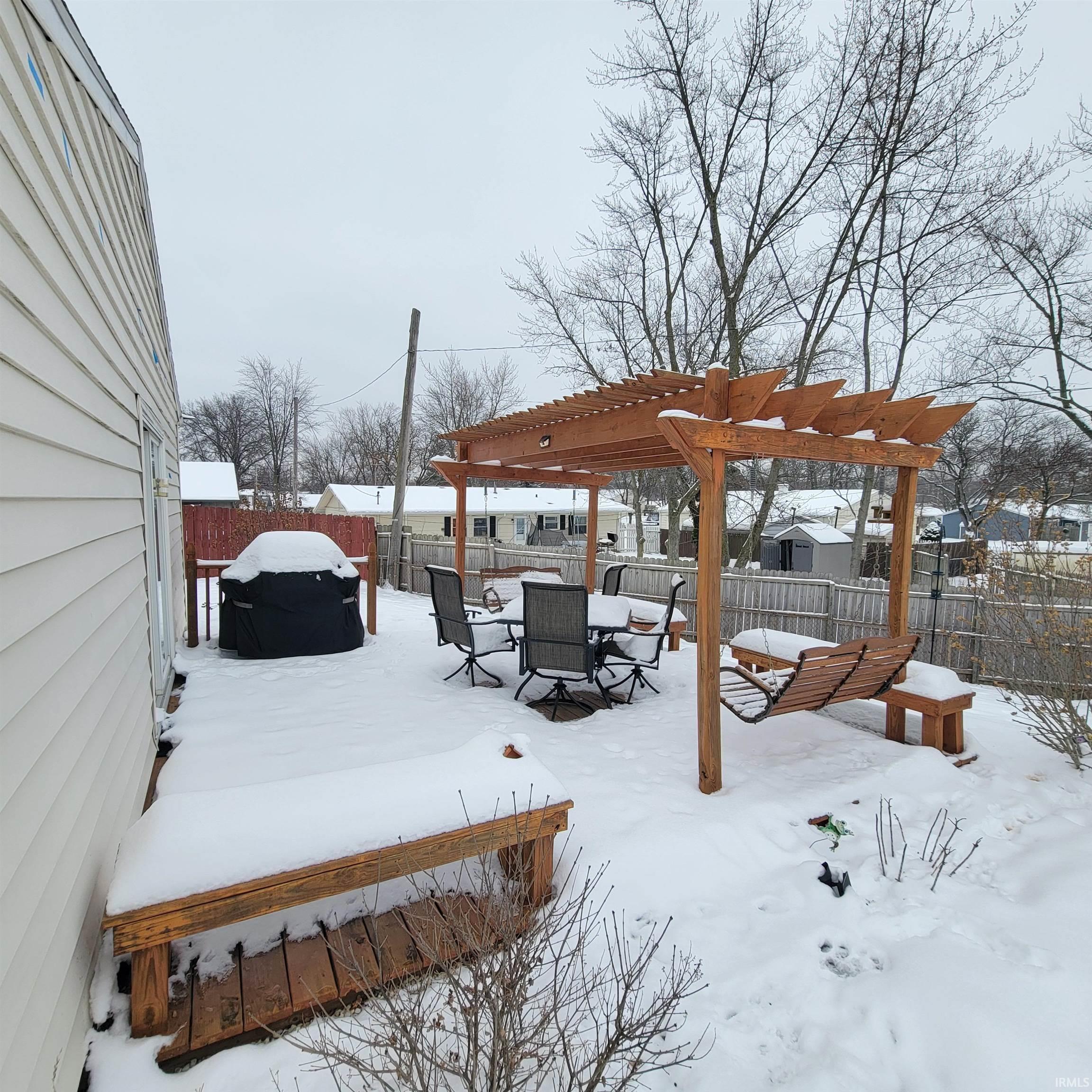 Yard covered in snow featuring a fenced backyard and a pergola
