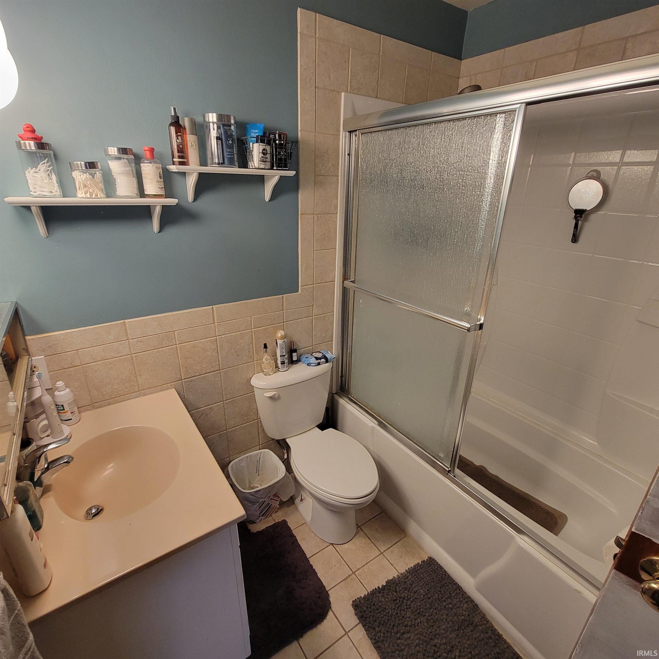 Full bathroom featuring tile walls, vanity, combined bath / shower with glass door, wainscoting, and light tile patterned floors