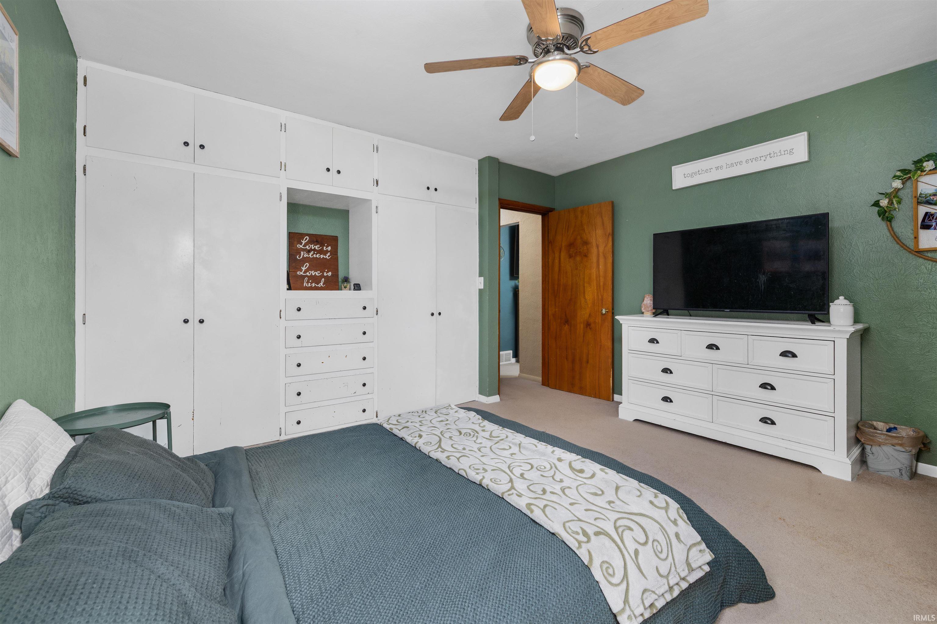 Carpeted bedroom with a ceiling fan and multiple closets