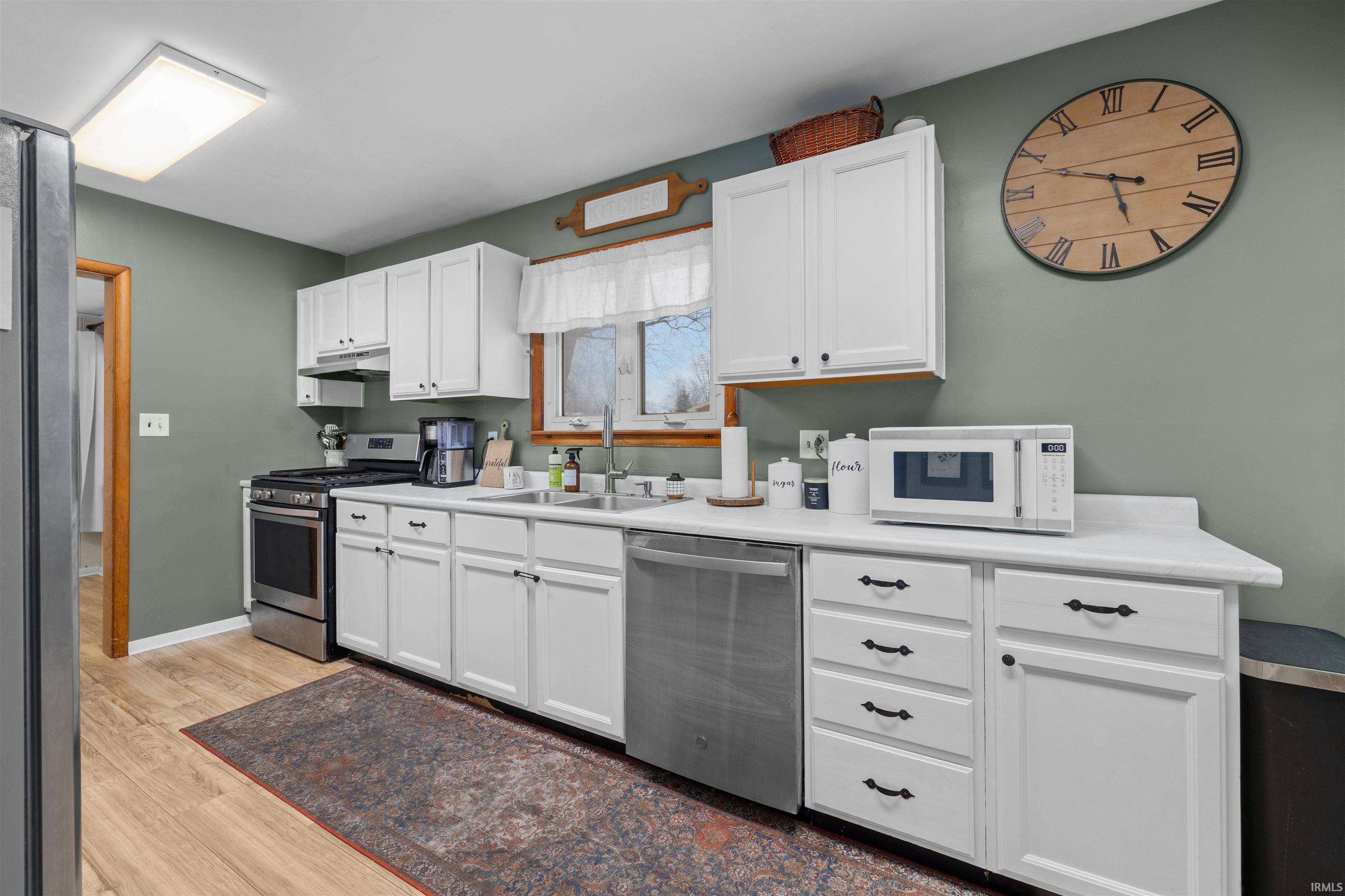 Kitchen with white cabinetry, appliances with stainless steel finishes, light countertops, light wood finished floors, and under cabinet range hood