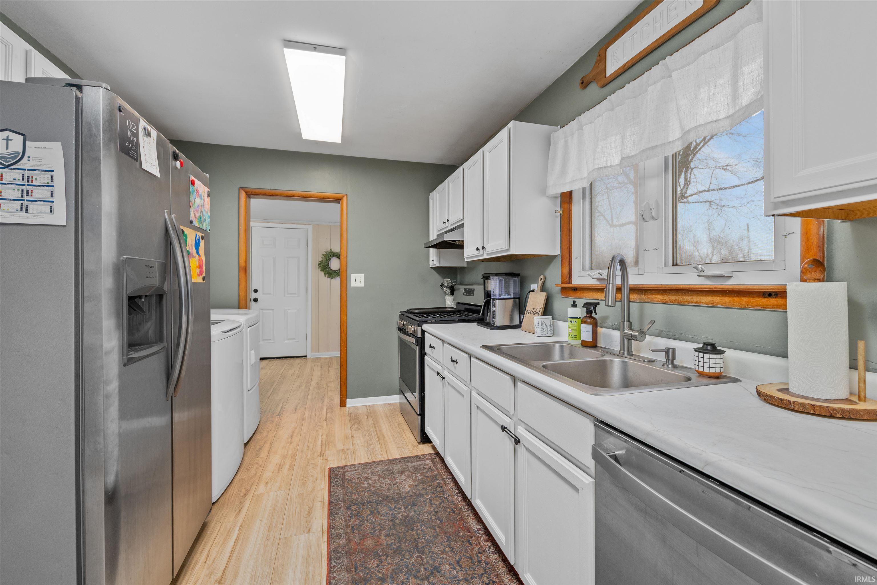 Kitchen featuring appliances with stainless steel finishes, white cabinetry, light wood-style floors, light countertops, and washer and dryer