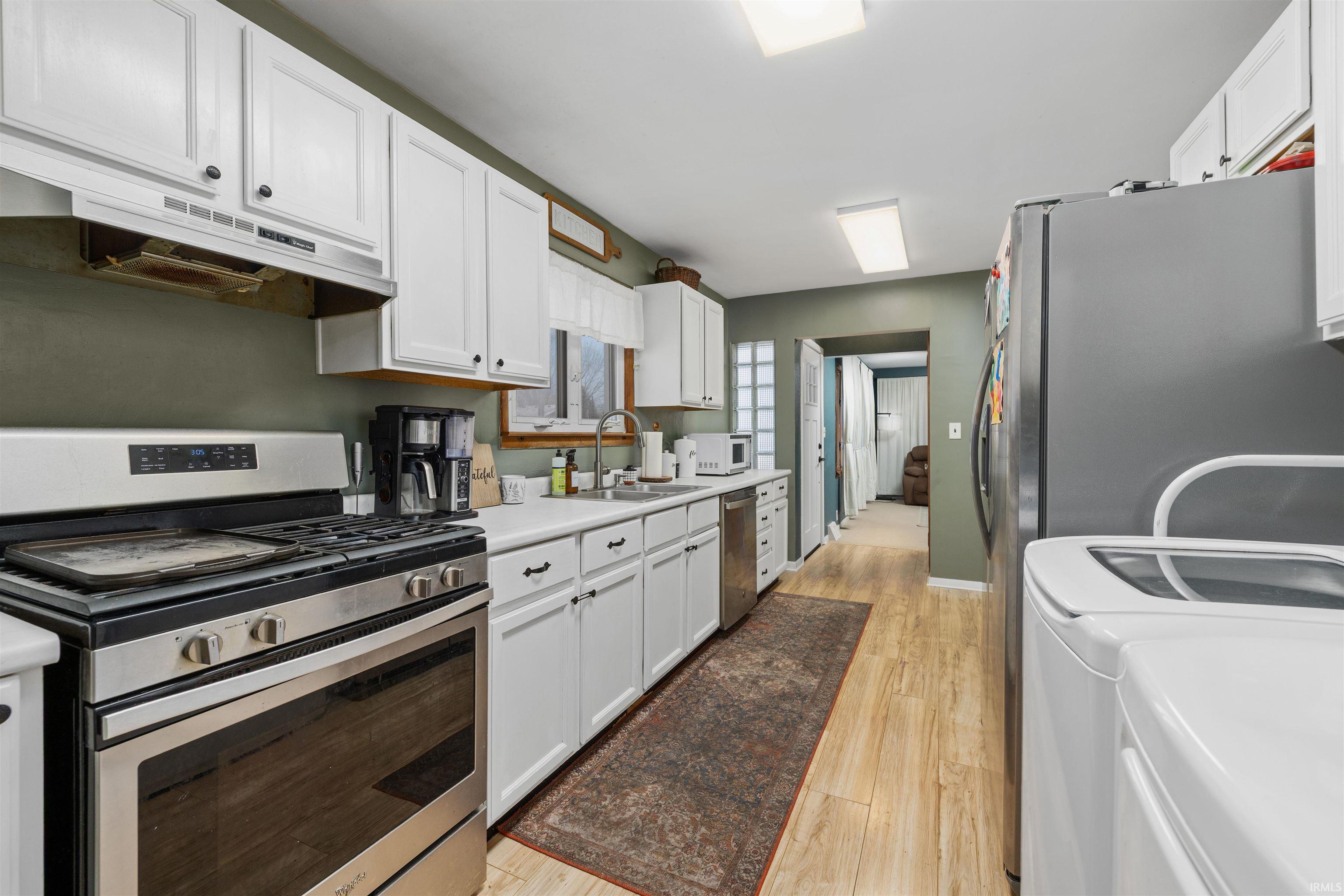 Kitchen with stainless steel appliances, white cabinets, under cabinet range hood, light countertops, and separate washer and dryer