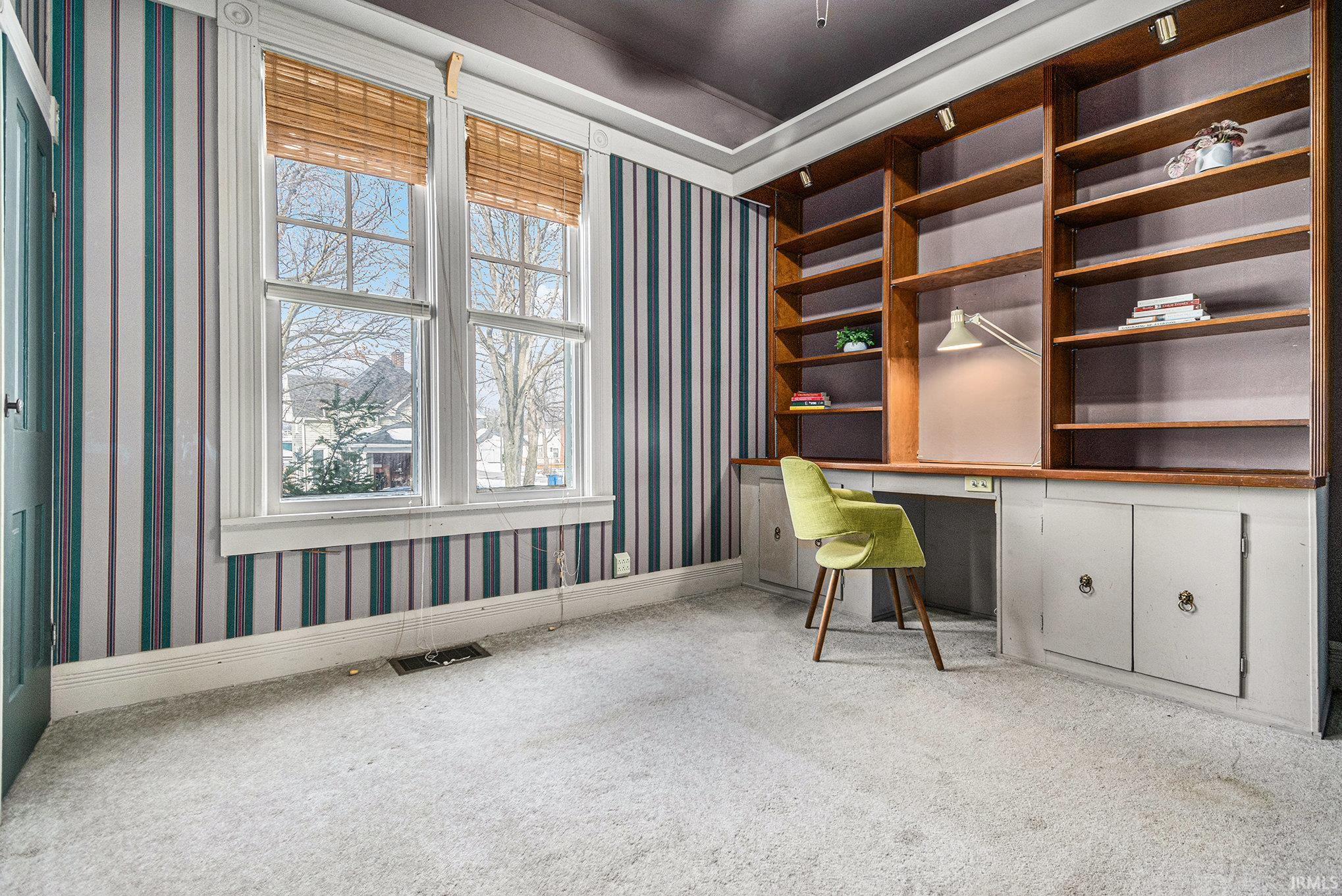 Carpeted office featuring built in study area and wallpapered walls