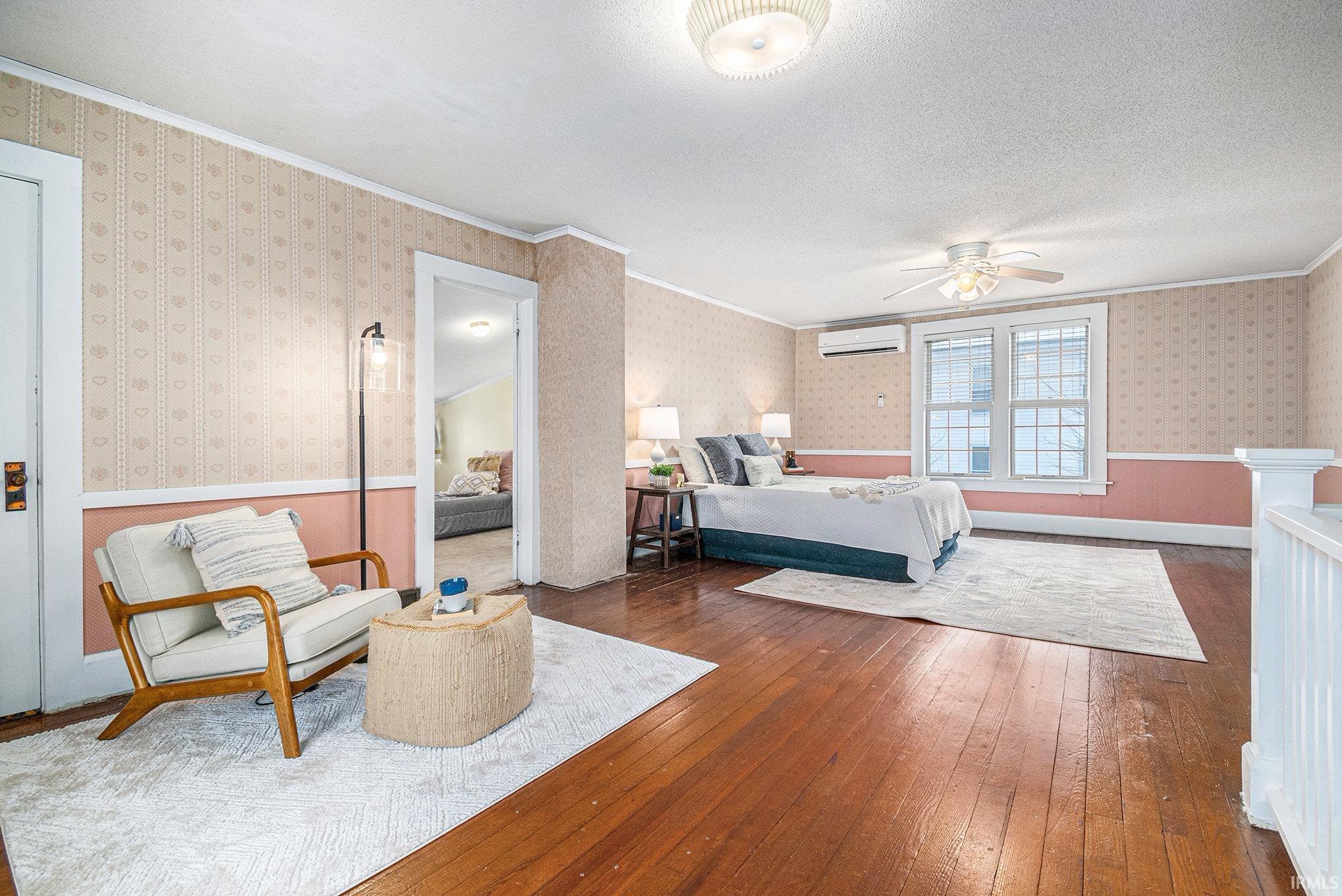 Bedroom with hardwood / wood-style floors, wallpapered walls, ceiling fan, a textured ceiling, and a wall unit AC