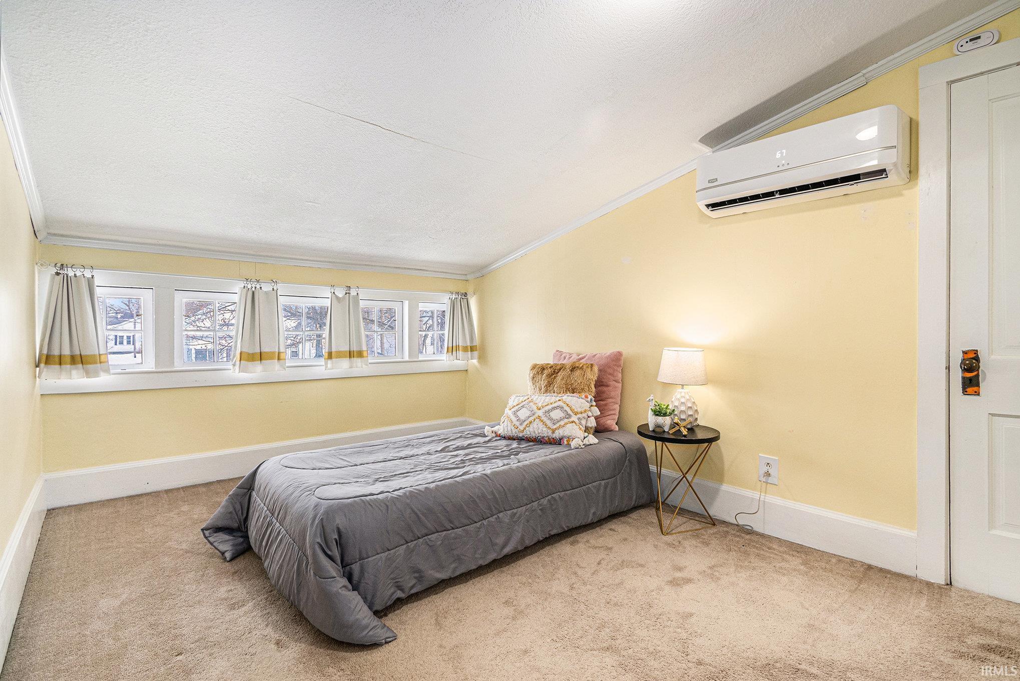Bedroom with carpet flooring, an AC wall unit, crown molding, and a textured ceiling