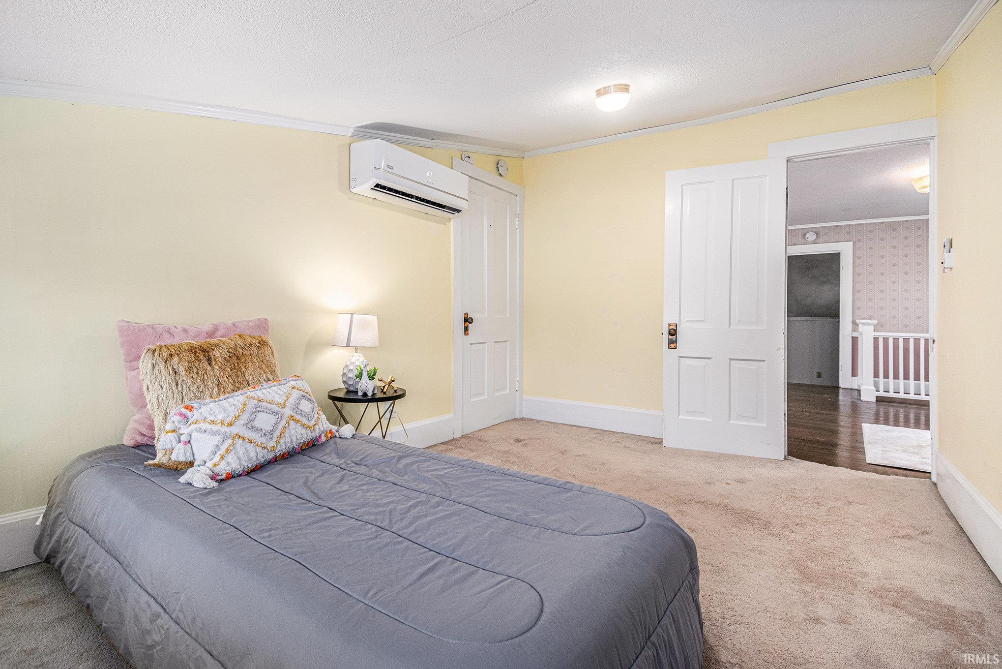 Bedroom featuring ornamental molding, carpet, a textured ceiling, and an AC wall unit
