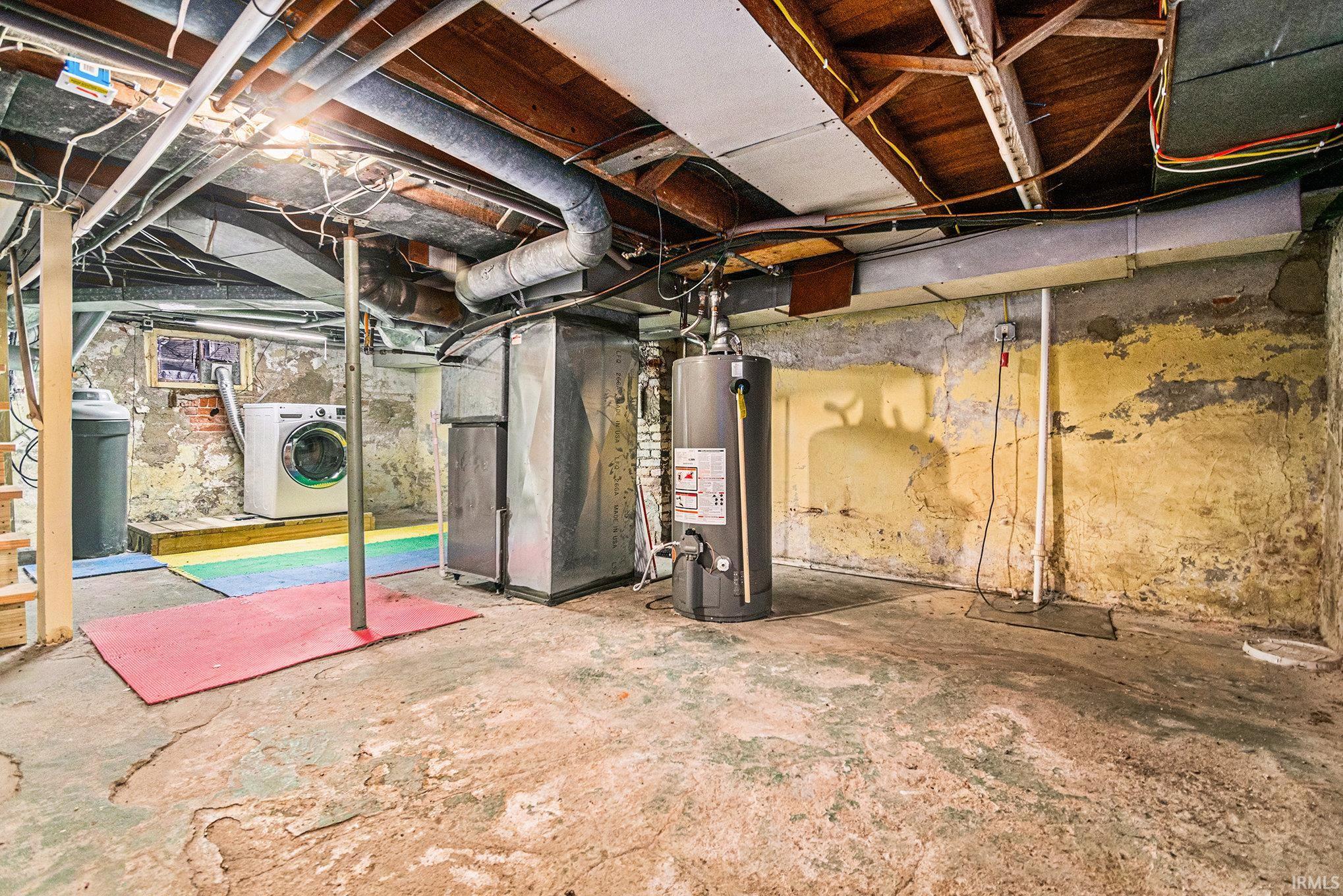 Unfinished basement featuring washer / clothes dryer, water heater, drainage system, and heating unit