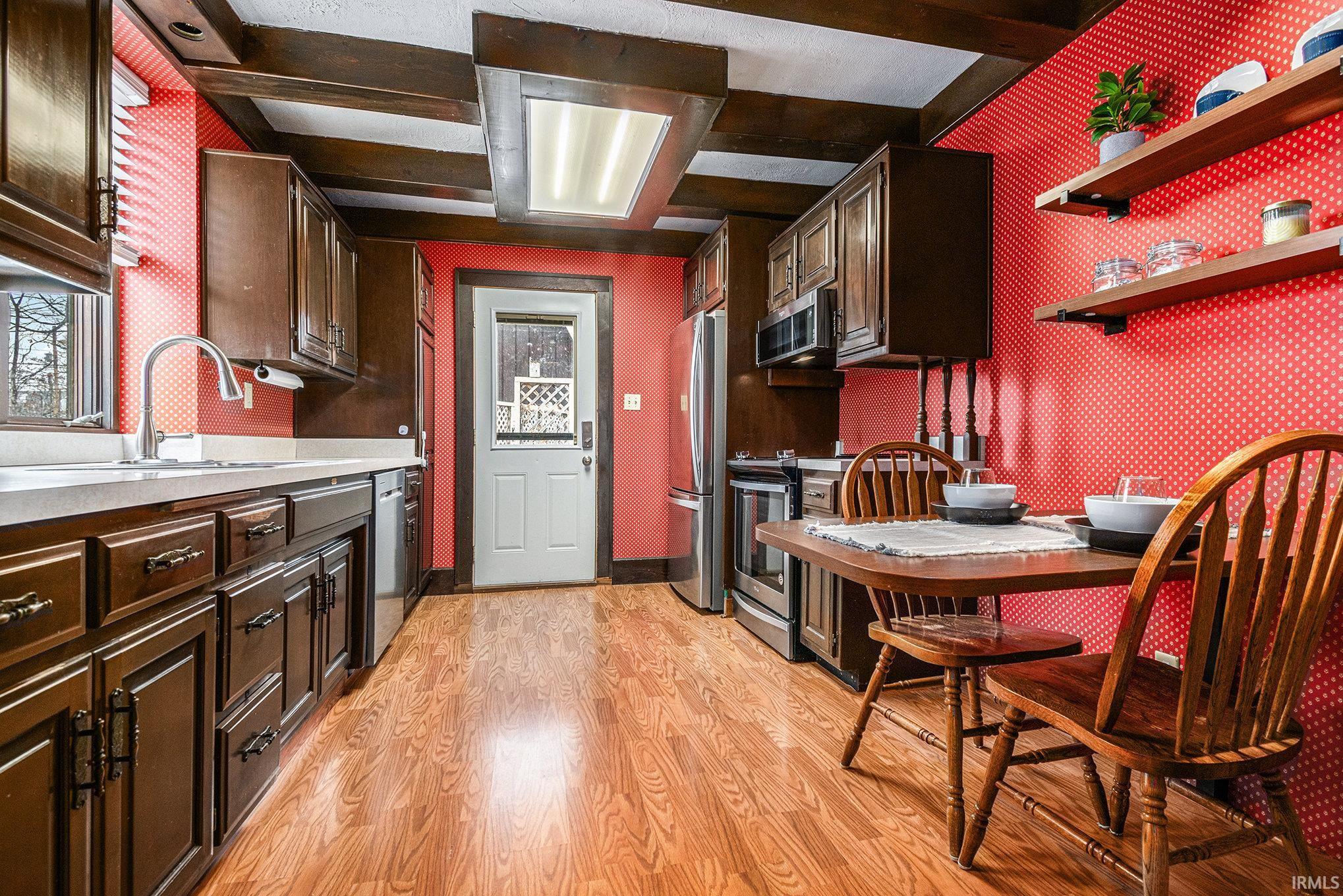 Kitchen with dark brown cabinetry, light countertops, light wood-style flooring, beamed ceiling, and wallpapered walls