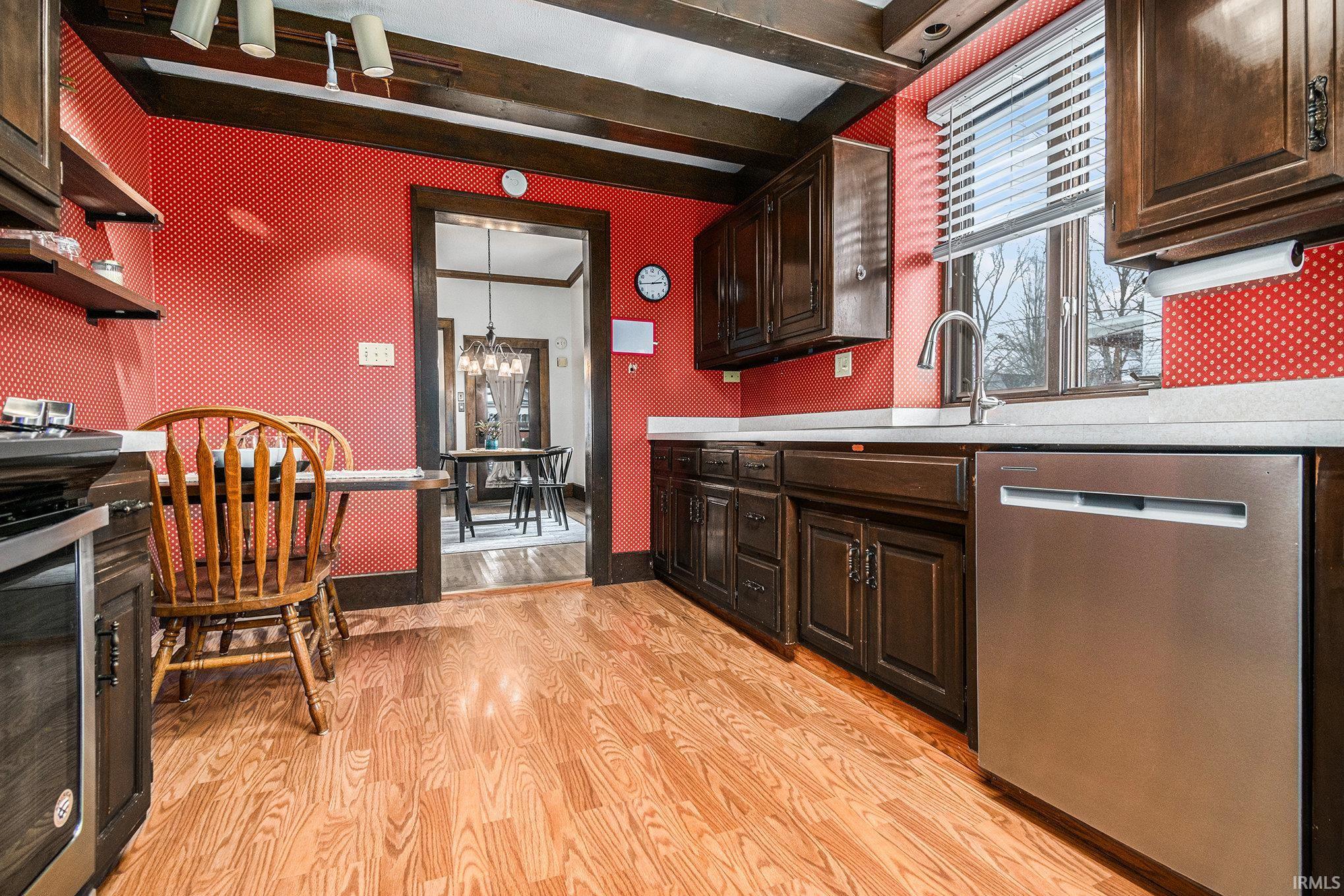 Kitchen with dark brown cabinetry, dishwasher, light countertops, beam ceiling, and light wood finished floors