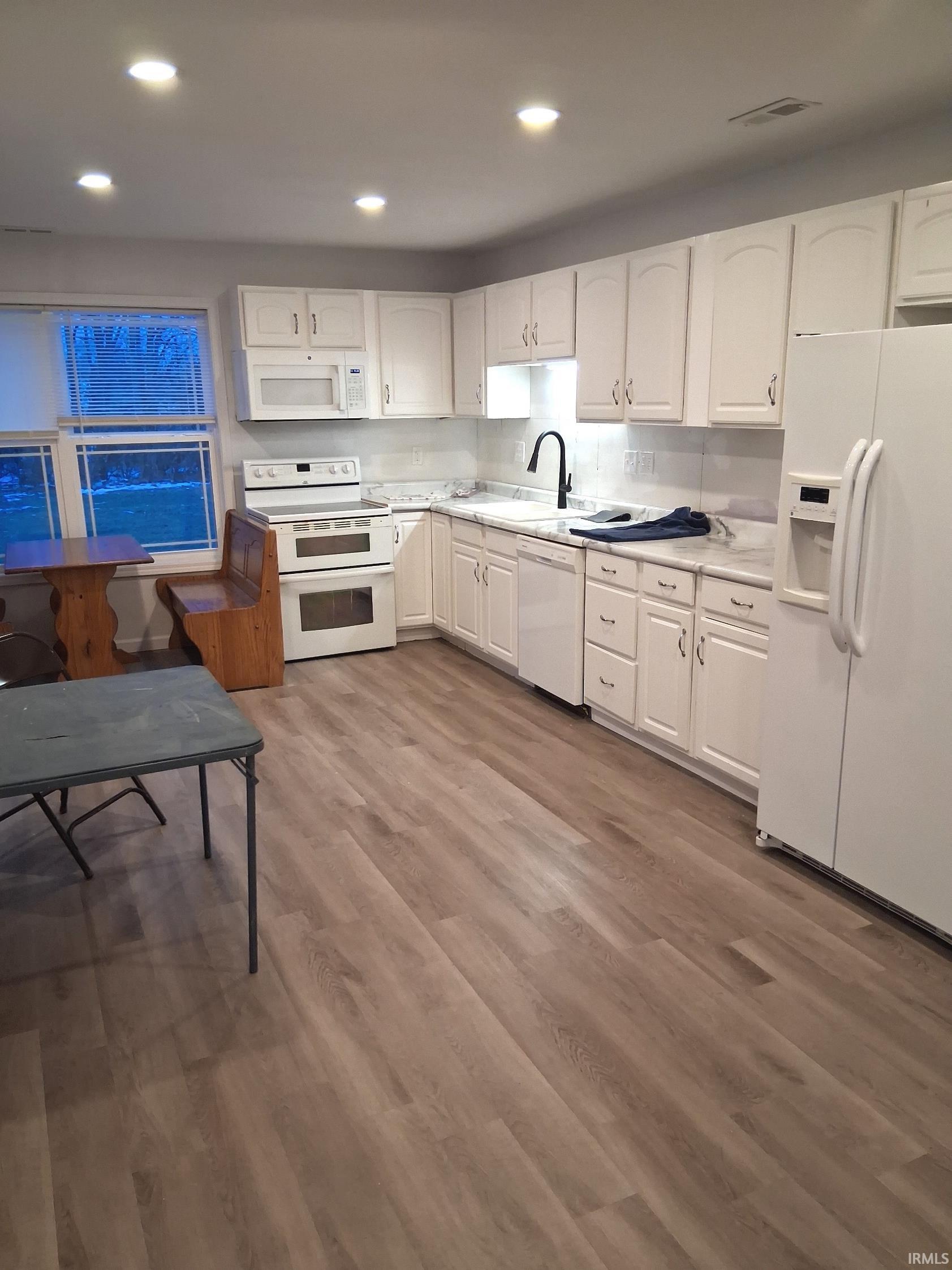 Kitchen with white appliances, white cabinets, light countertops, recessed lighting, and dark wood-type flooring
