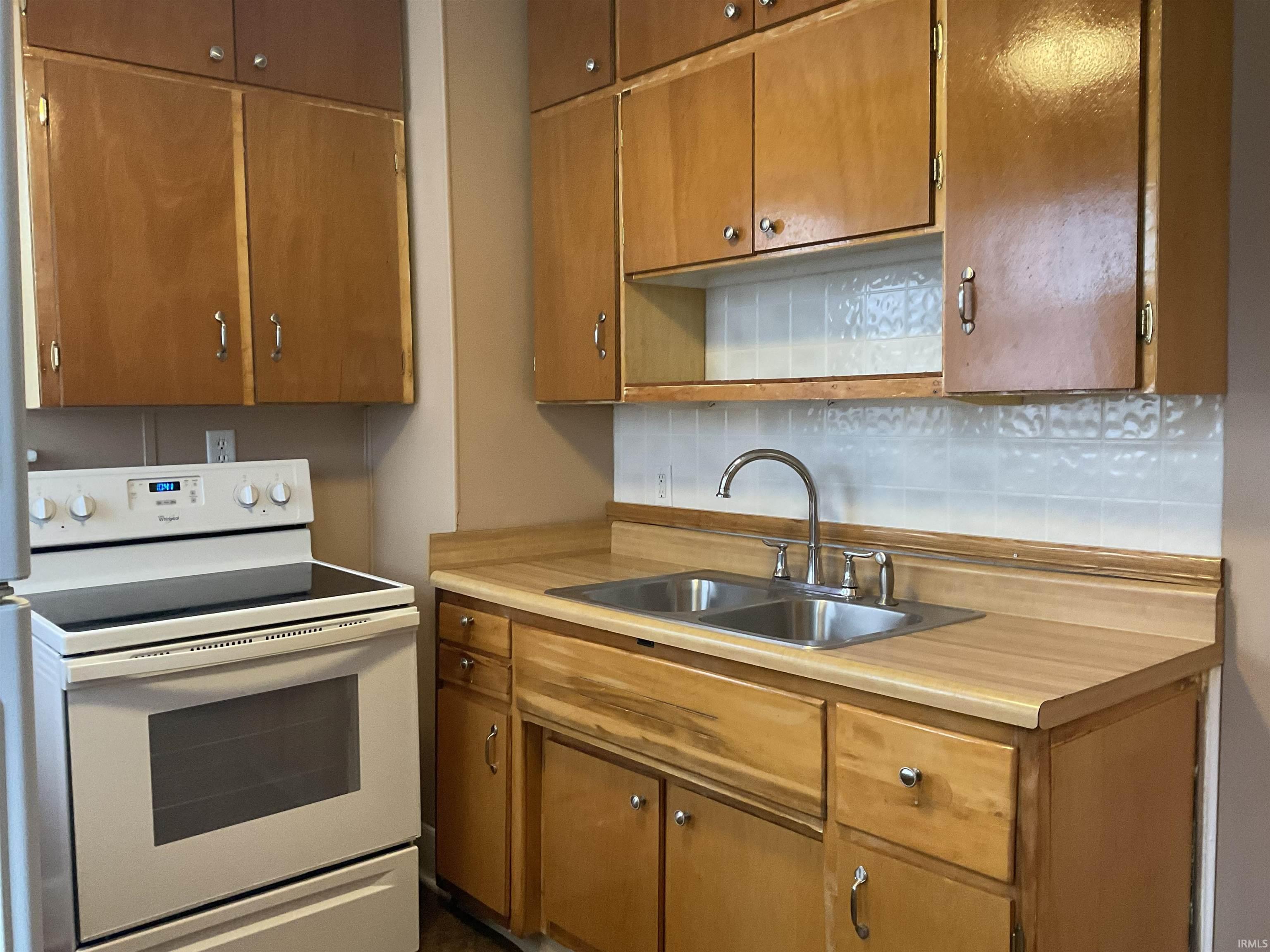 Kitchen featuring electric stove, light countertops, brown cabinetry, and tasteful backsplash