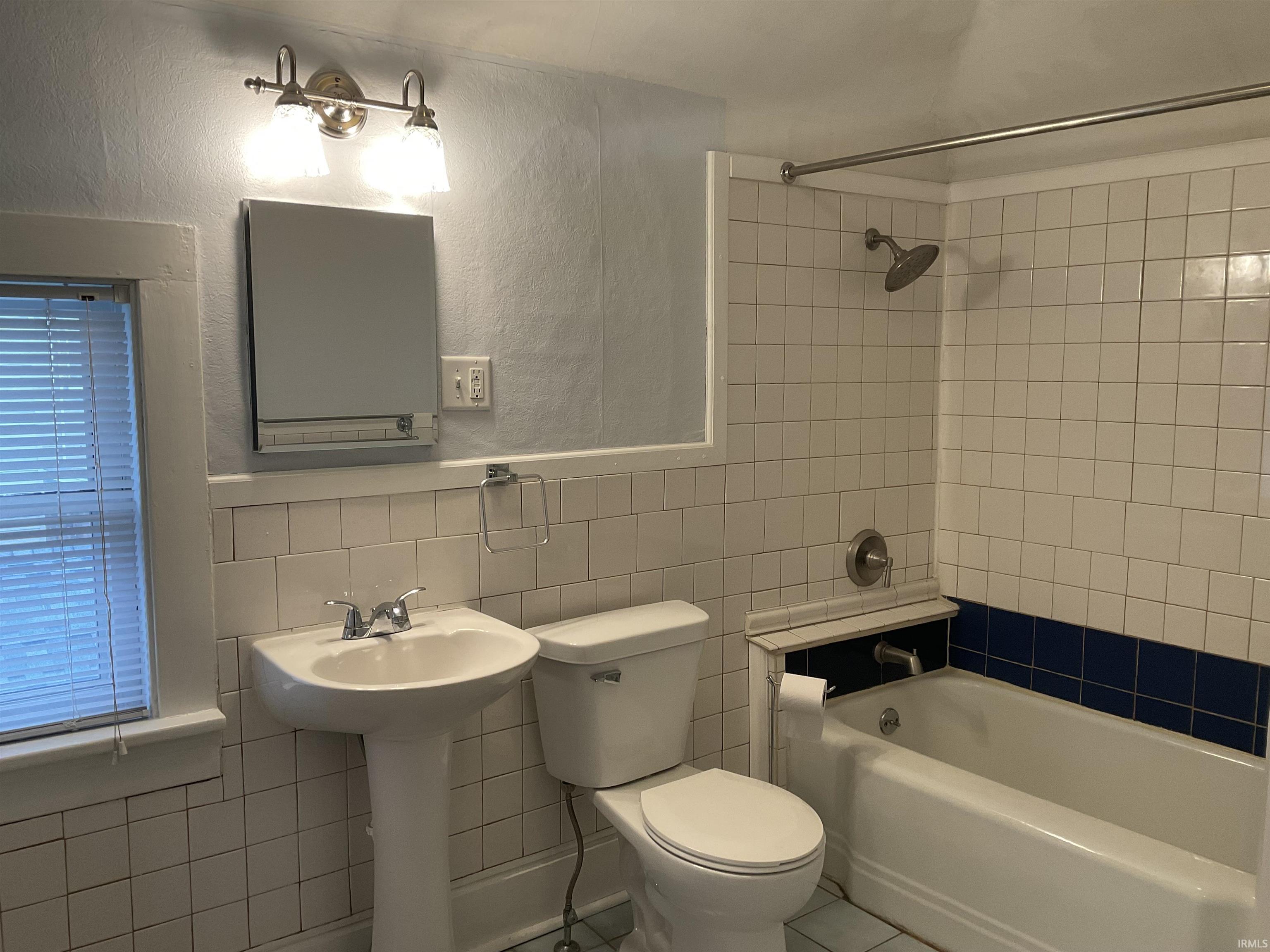 Bathroom with tile walls, a textured wall, shower / bath combination, a wainscoted wall, and tile patterned floors
