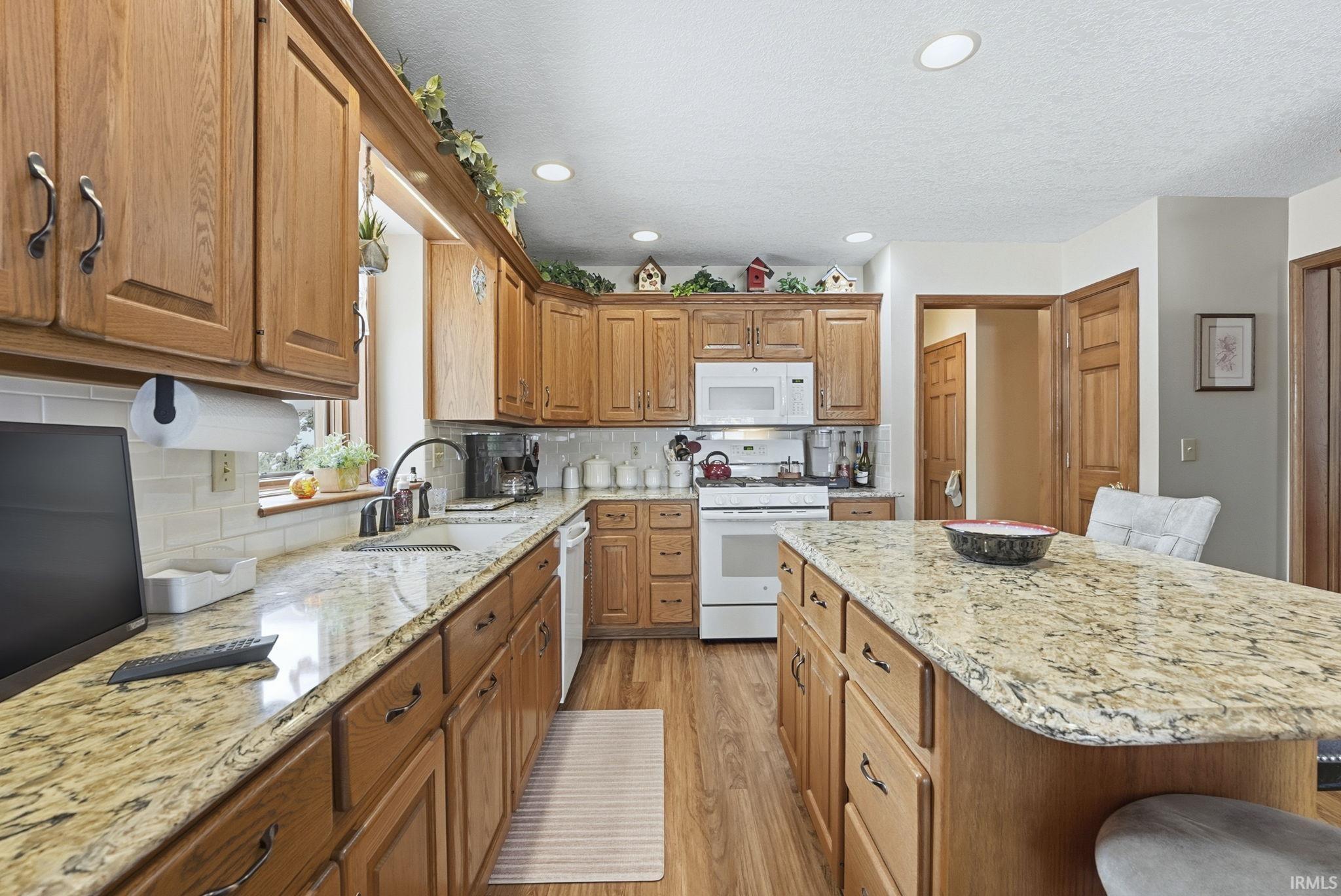 Kitchen featuring a breakfast bar, light wood-type flooring, light stone countertops, white appliances, and a center island