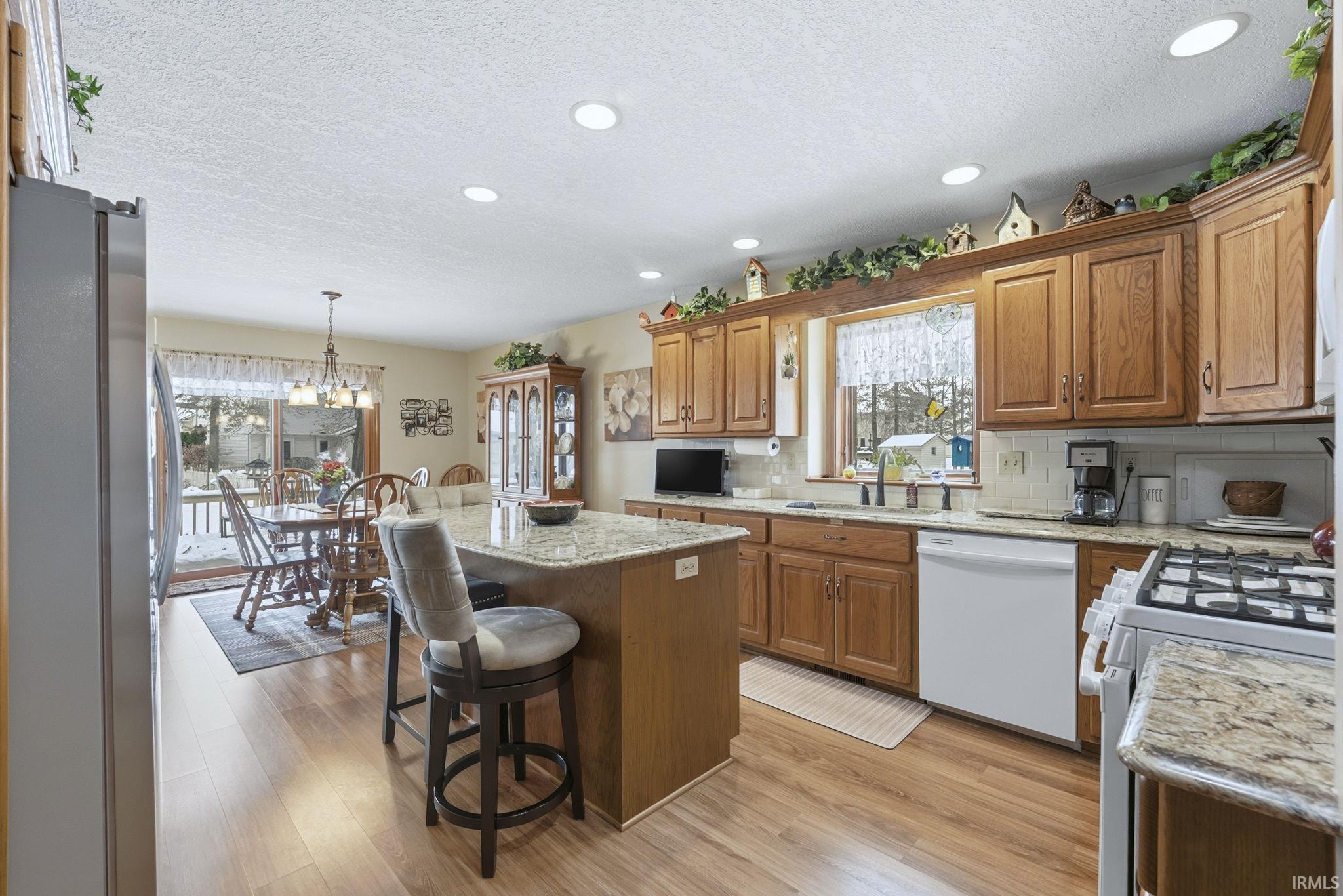 Kitchen with brown cabinetry, white appliances, a center island, a textured ceiling, and decorative light fixtures