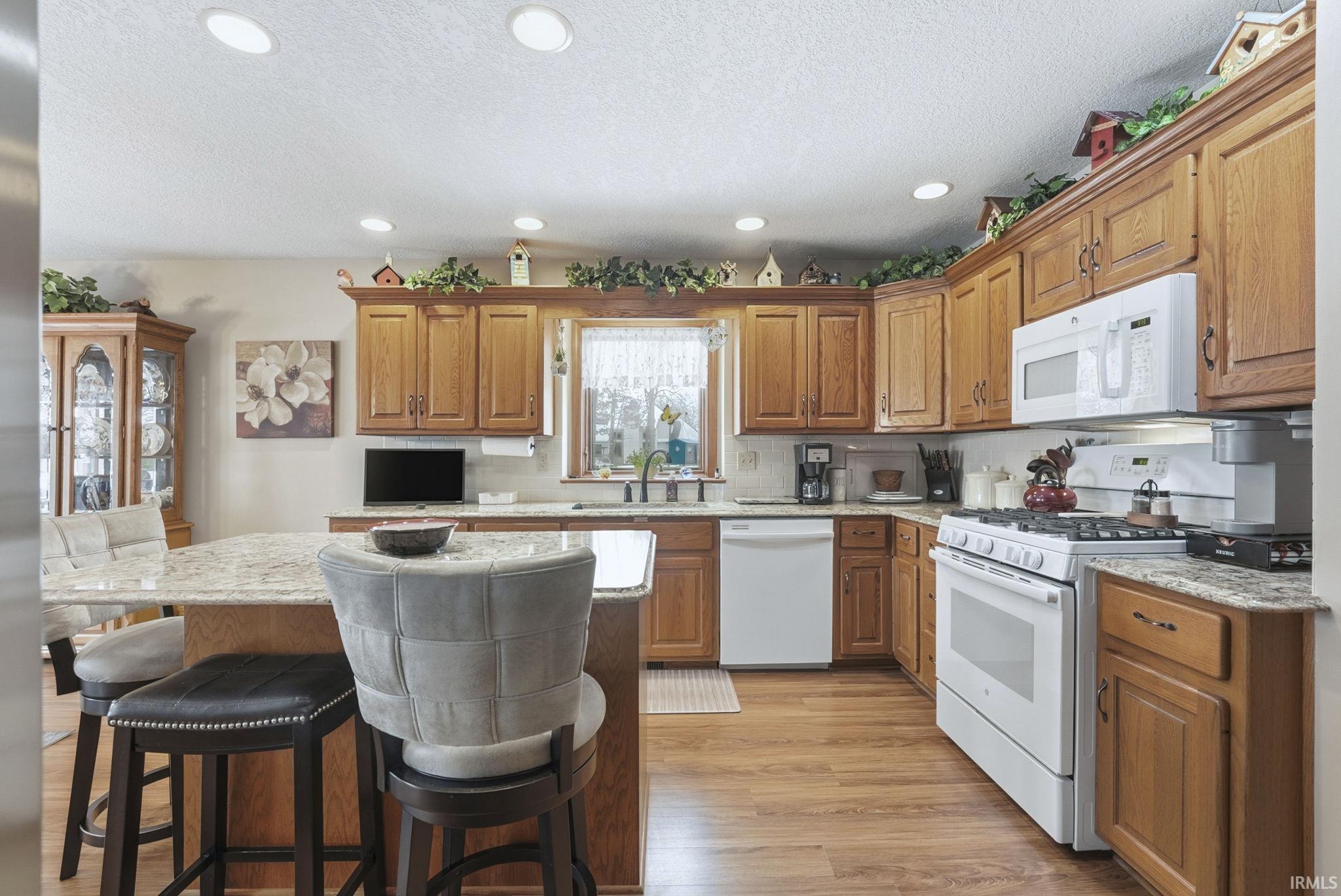 Kitchen with white appliances, brown cabinets, light stone counters, a kitchen island, and recessed lighting