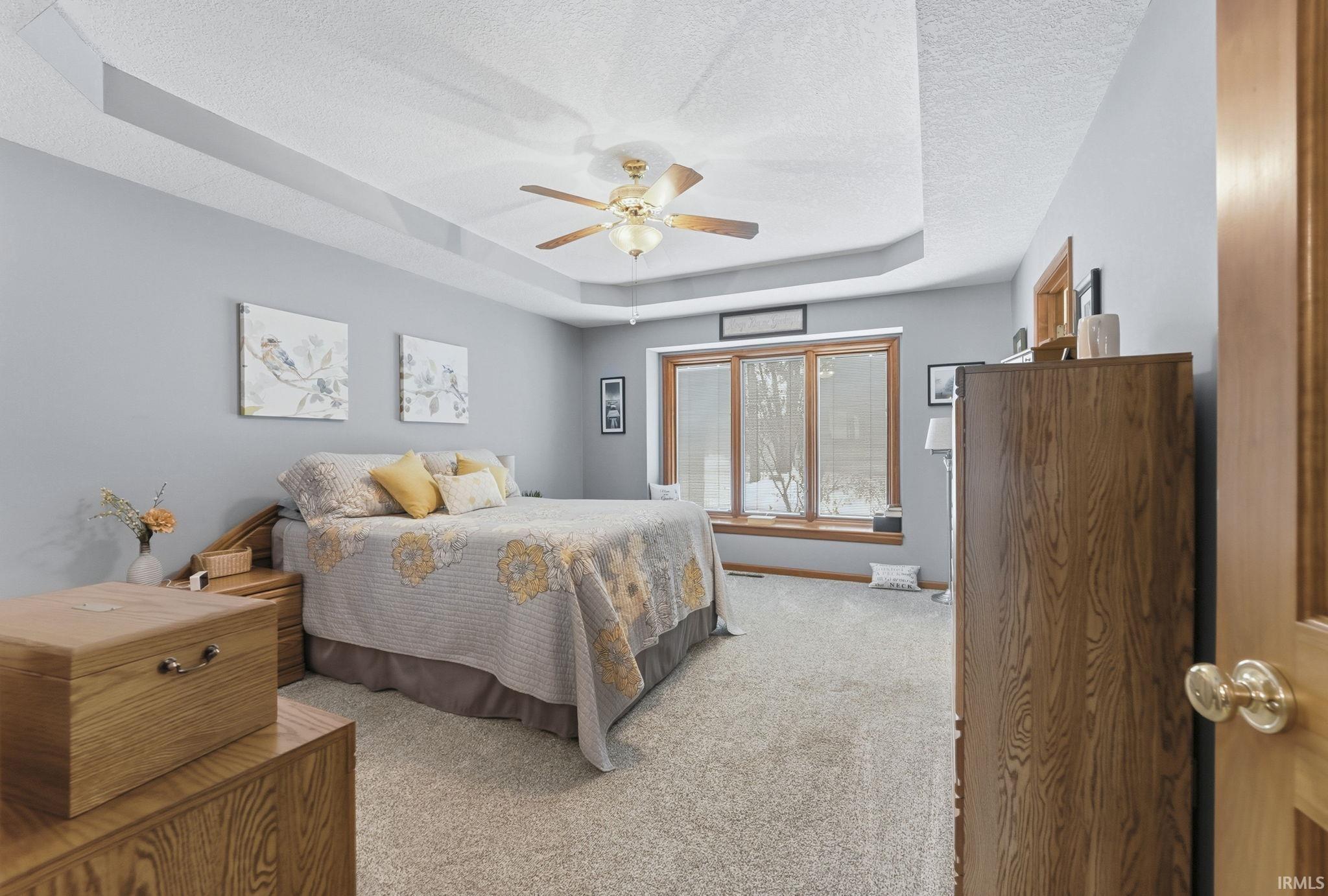 Bedroom featuring a tray ceiling, carpet floors, a ceiling fan, and a textured ceiling