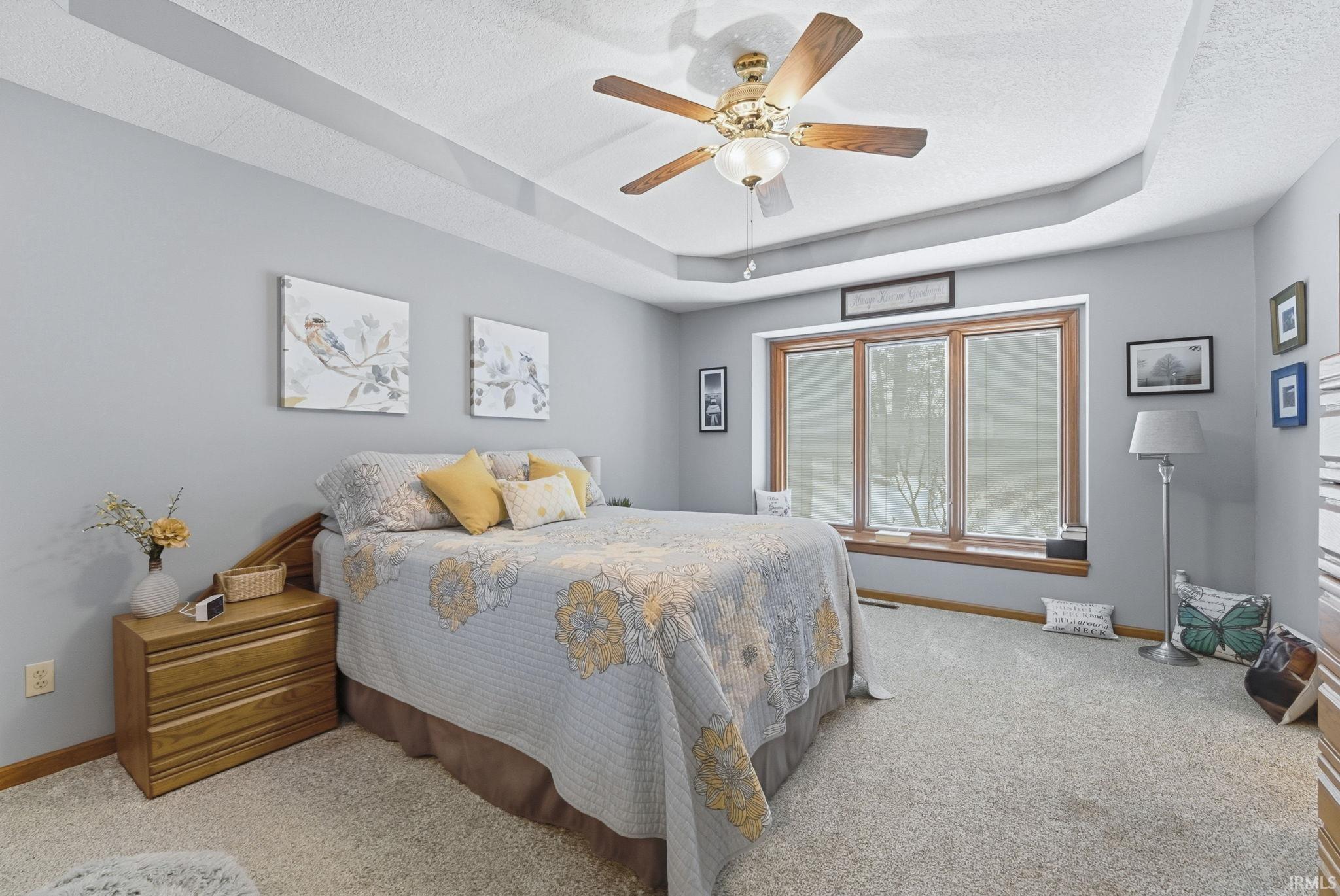 Carpeted bedroom with a raised ceiling, ceiling fan, and a textured ceiling