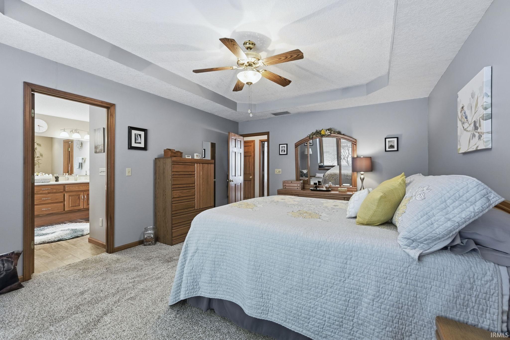 Bedroom with a tray ceiling, light colored carpet, a ceiling fan, and ensuite bathroom