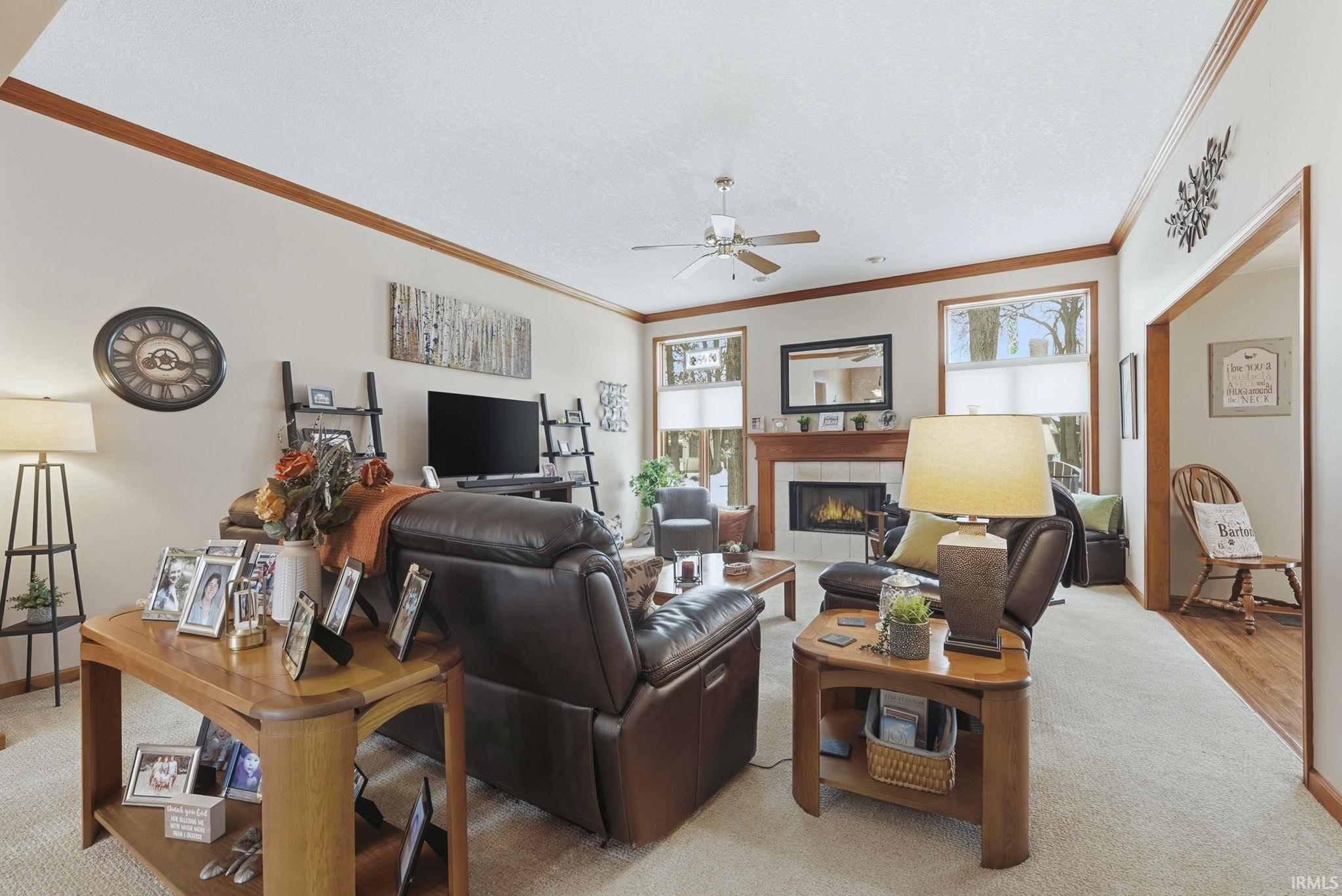Living area with a tiled fireplace, ornamental molding, a textured ceiling, ceiling fan, and light carpet