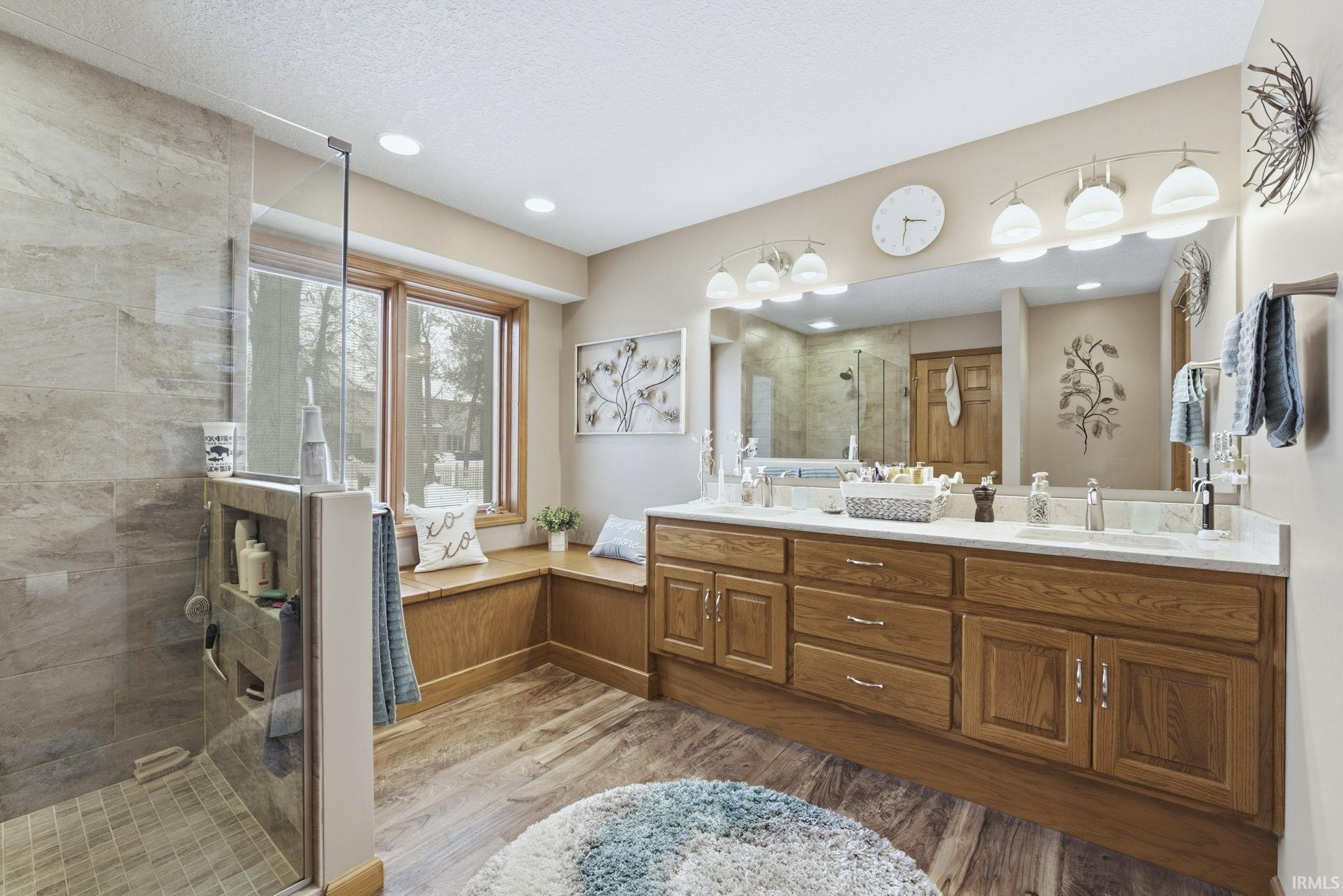 Bathroom featuring double vanity, a stall shower, light wood-style flooring, and a textured ceiling