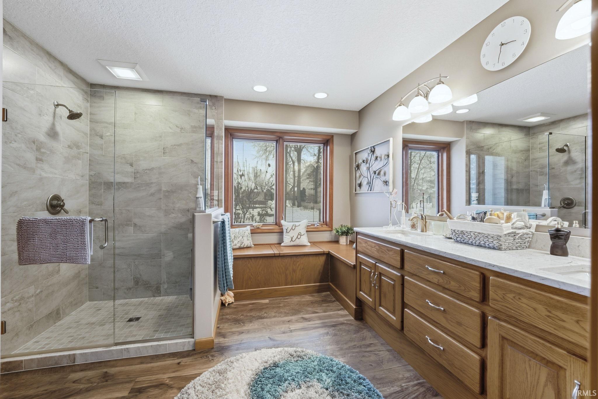 Bathroom featuring double vanity, a shower stall, dark wood-style flooring, and a textured ceiling