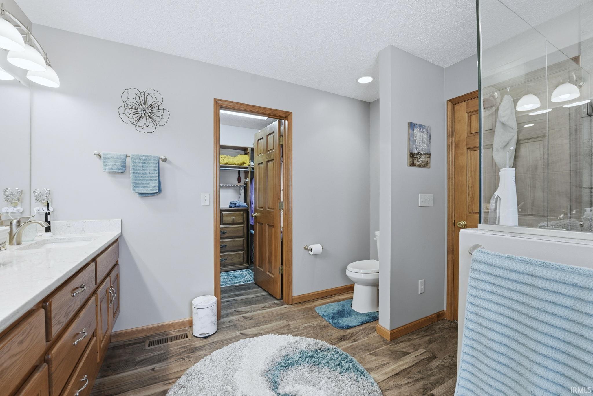 Bathroom featuring a spacious closet, vanity, light wood finished floors, a textured ceiling, and a shower with shower door