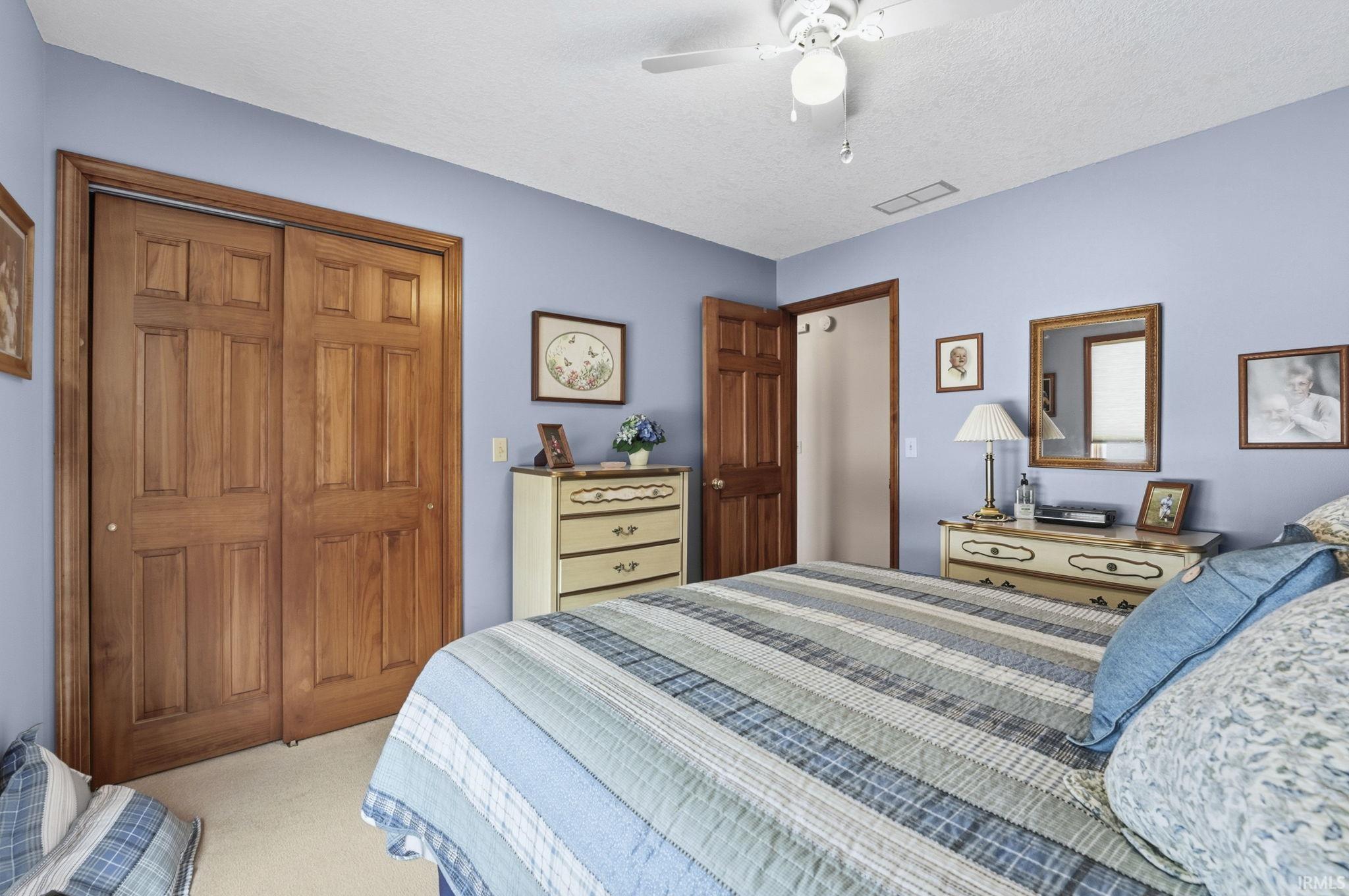 Bedroom with a closet, ceiling fan, light colored carpet, and a textured ceiling