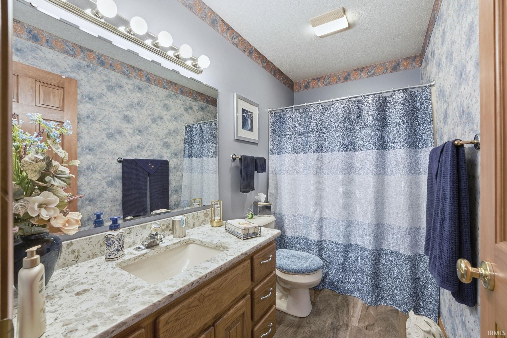Bathroom with a shower with shower curtain, vanity, a textured ceiling, wallpapered walls, and dark wood-style floors