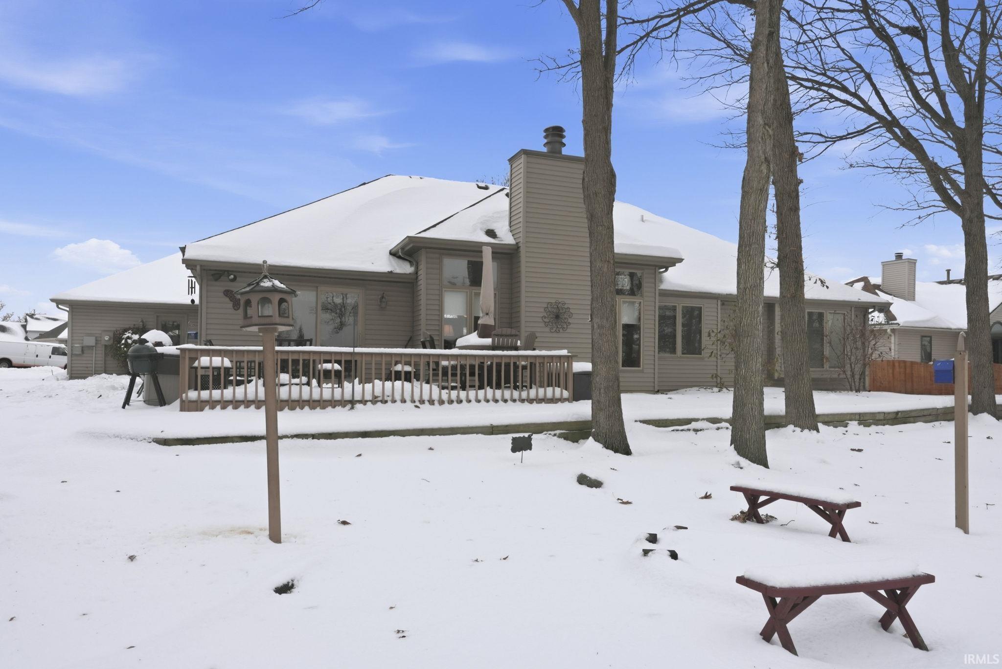 Snow covered back of property featuring a deck and a chimney