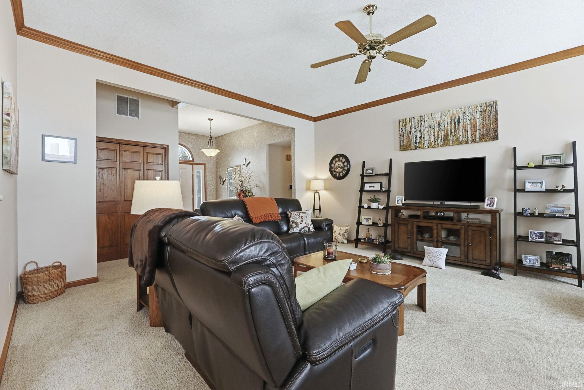 Living area featuring ornamental molding, light carpet, and a ceiling fan