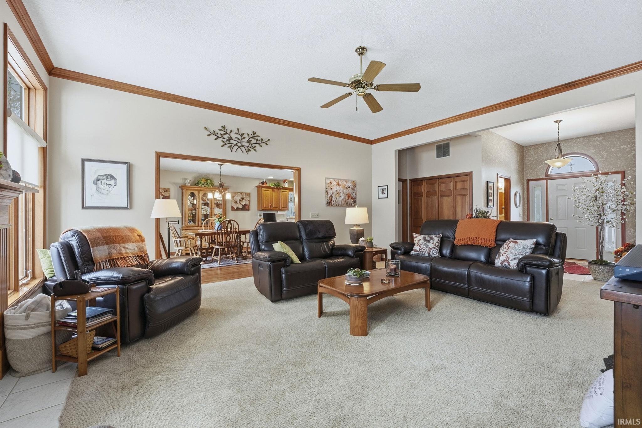 Living area with ornamental molding, a ceiling fan, and light carpet