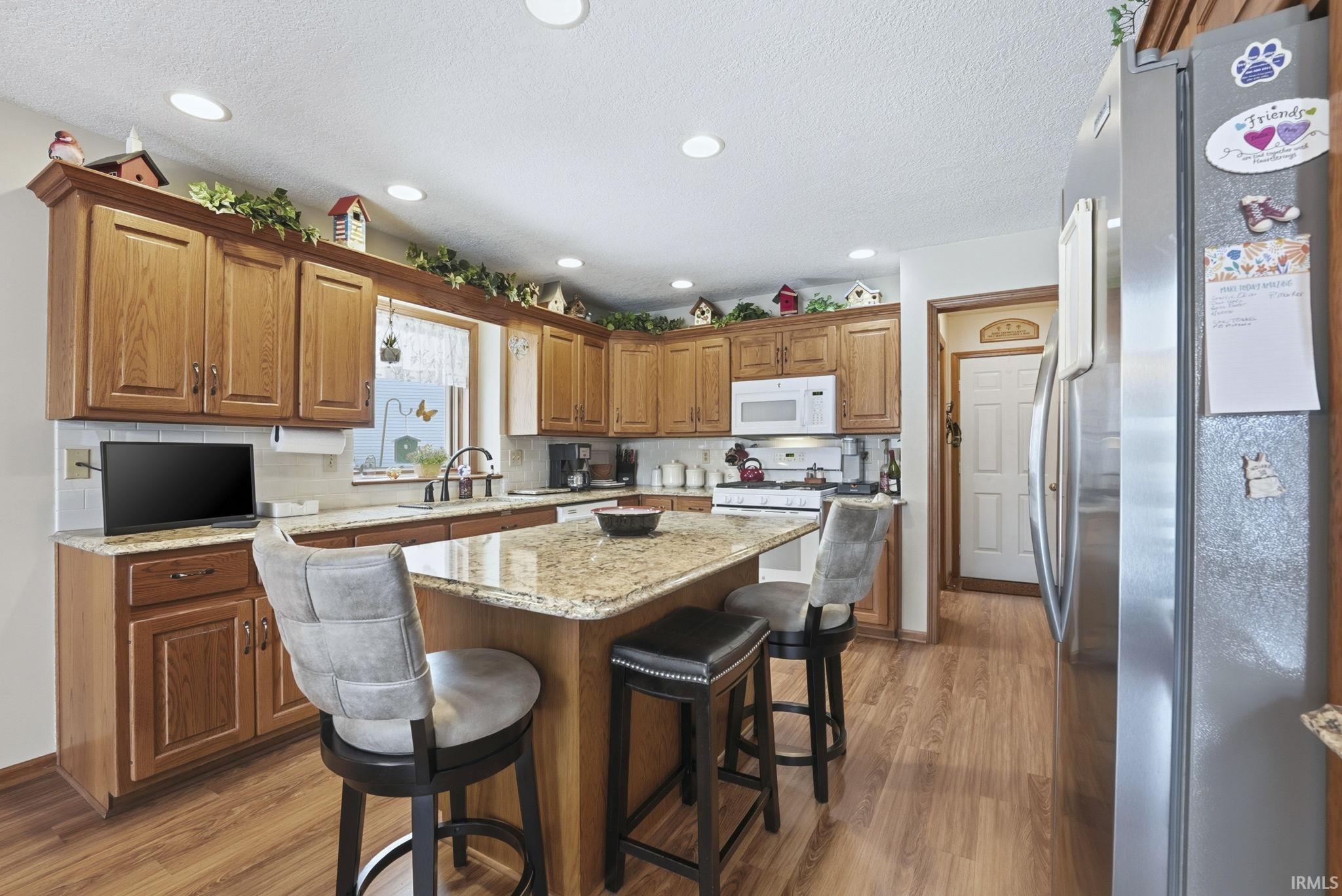 Kitchen with white appliances, brown cabinetry, a breakfast bar, light wood-style flooring, and a textured ceiling