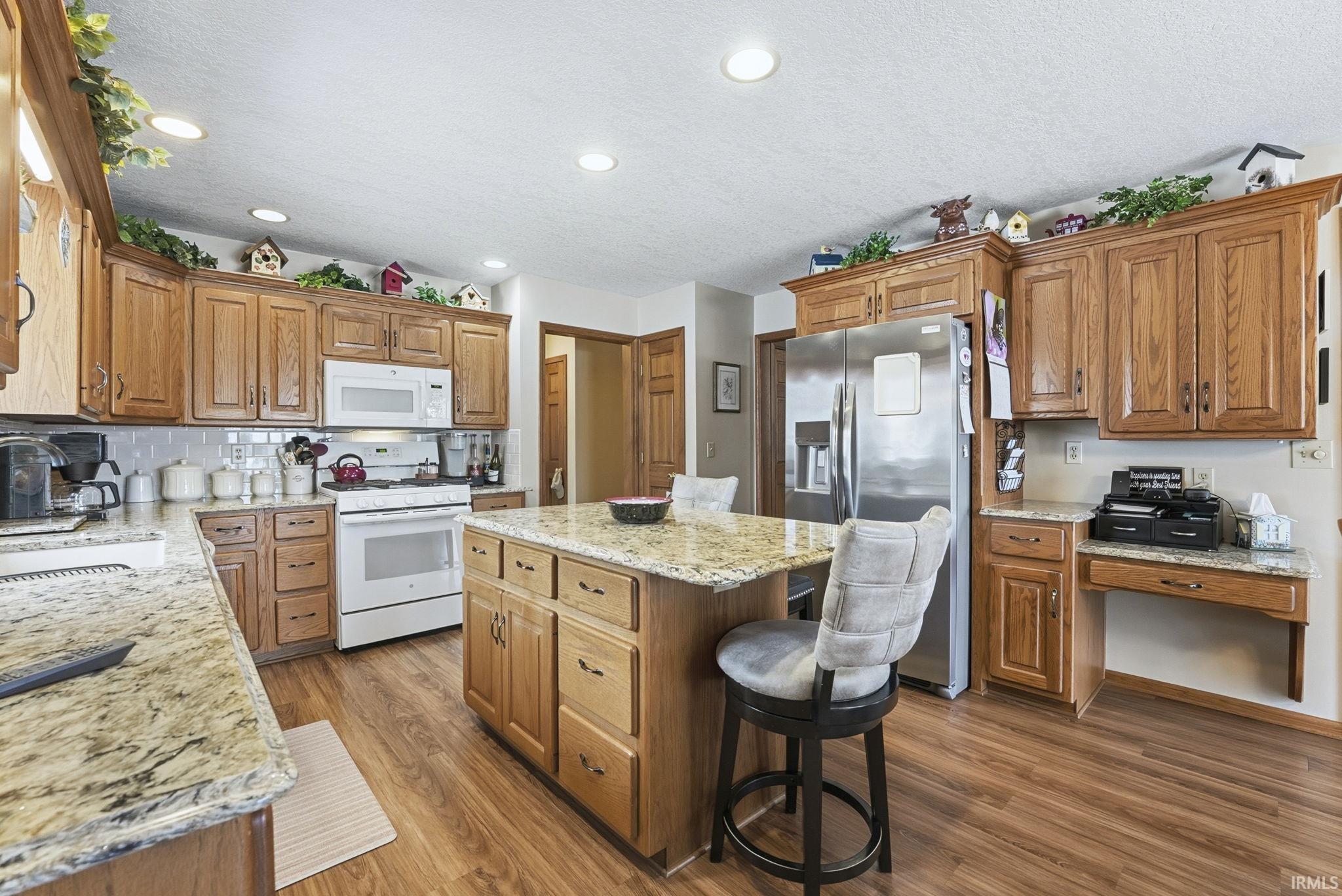 Kitchen featuring white appliances, brown cabinets, light stone countertops, dark wood-style flooring, and recessed lighting