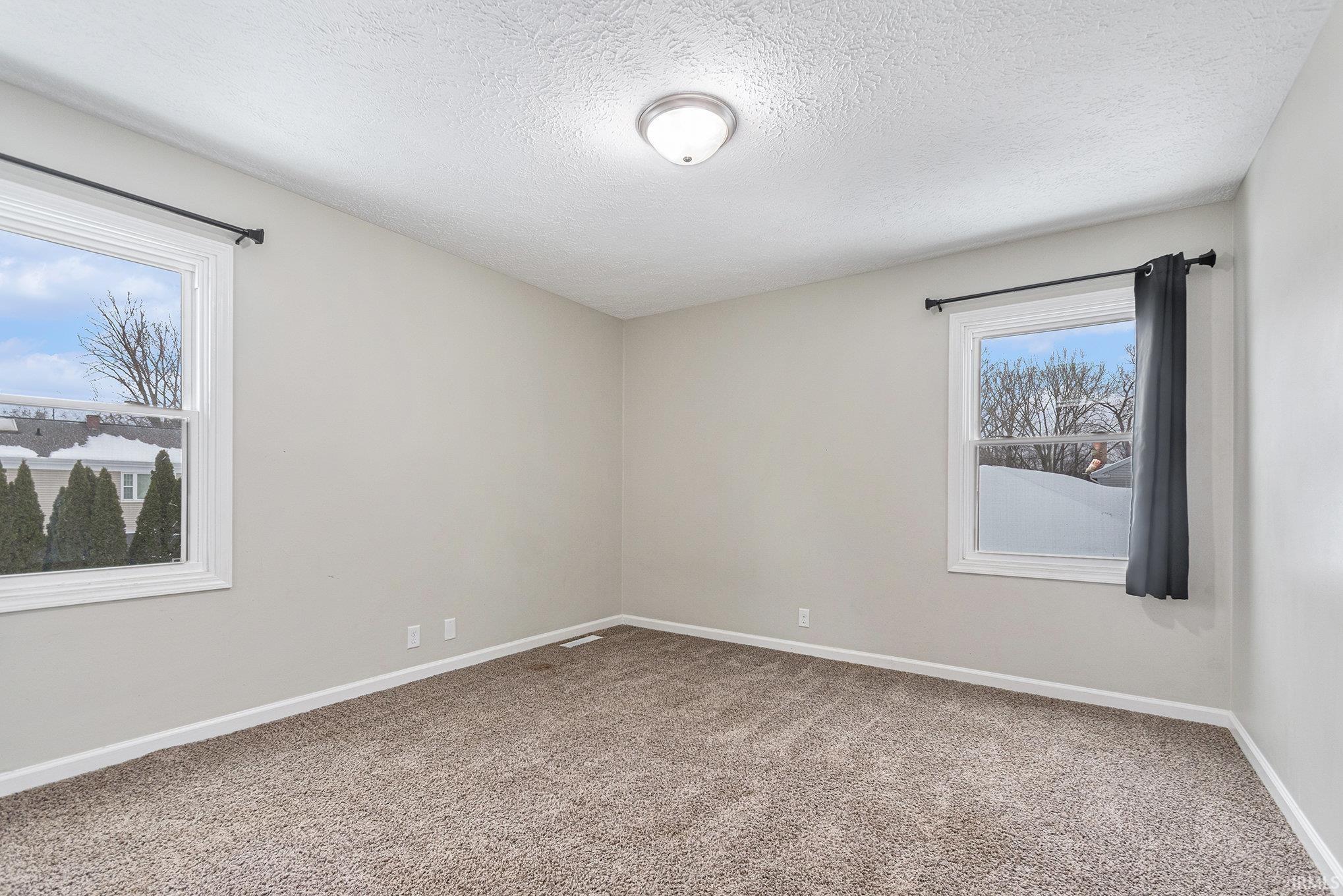 Unfurnished room featuring a textured ceiling, light colored carpet, and plenty of natural light