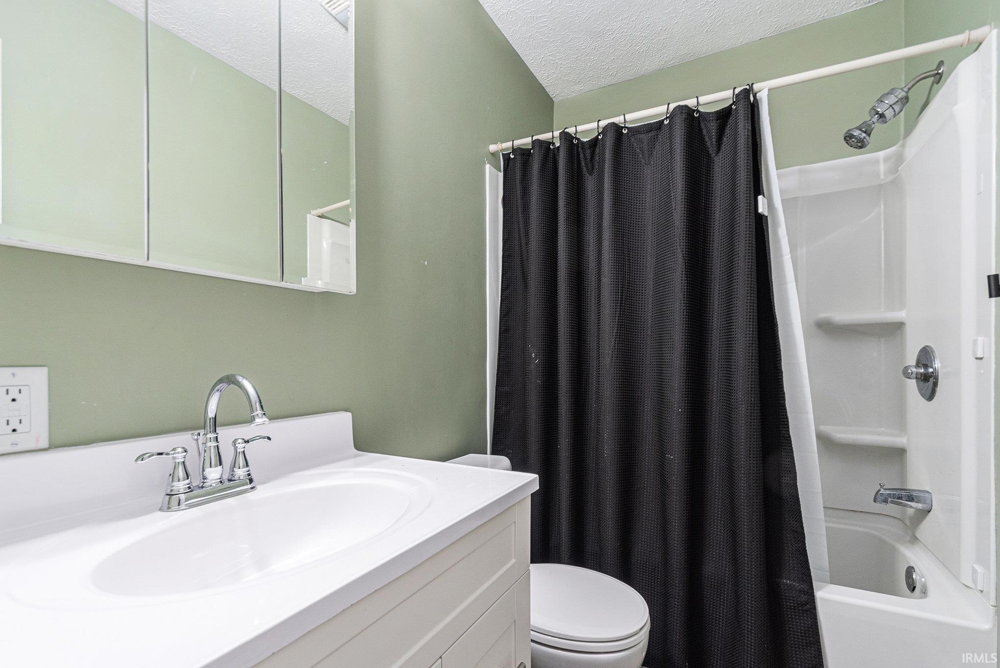 Full bathroom with shower / bath combo with shower curtain, a textured ceiling, and vanity
