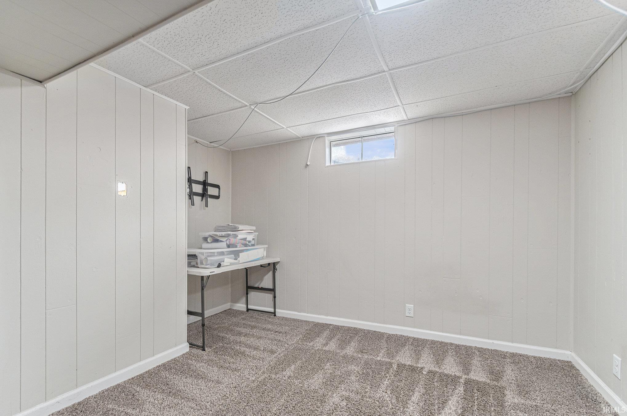 Below grade area featuring a drop ceiling, wooden walls, and light carpet