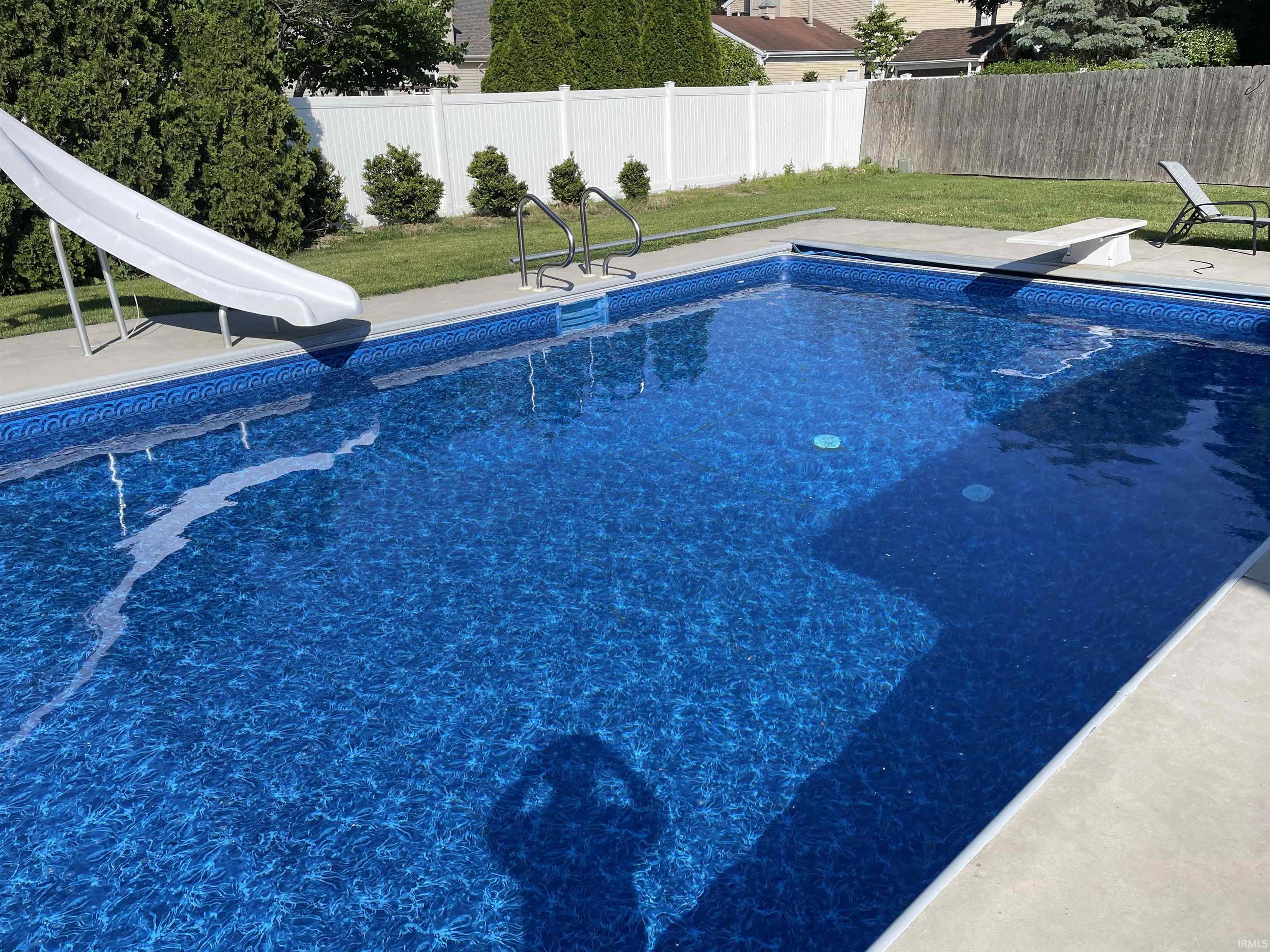 View of pool with a water slide, a fenced backyard, and a diving board
