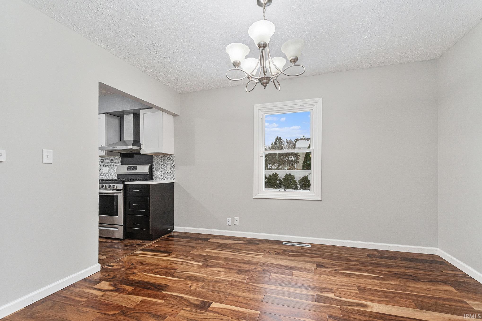 Unfurnished room with dark wood-style finished floors, a chandelier, and a textured ceiling