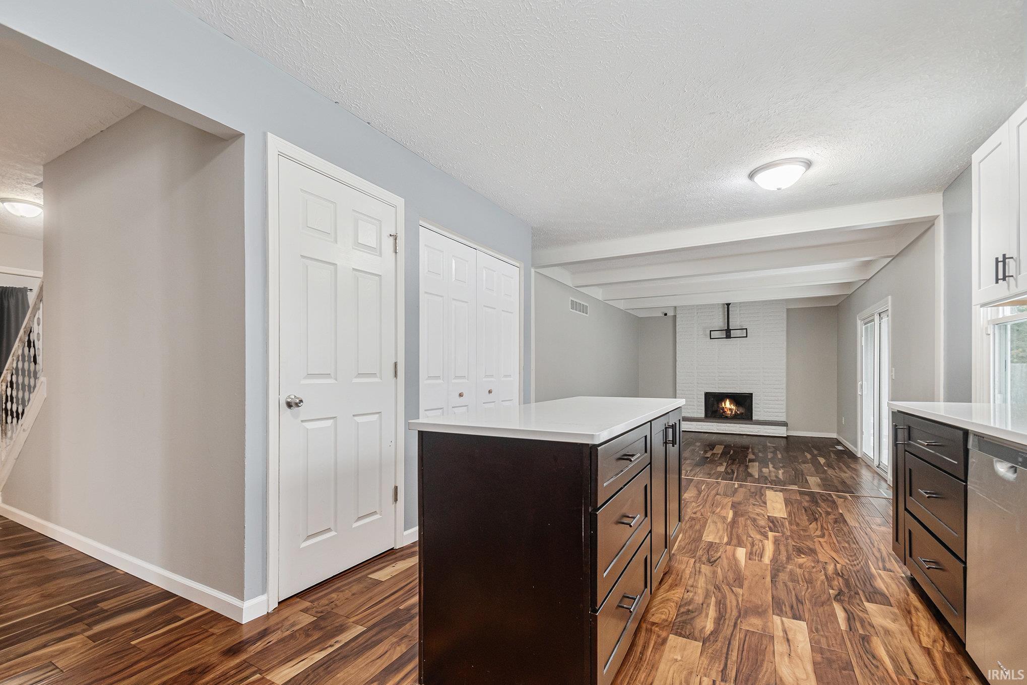 Kitchen with a center island, dark wood-style flooring, a brick fireplace, a textured ceiling, and dishwasher