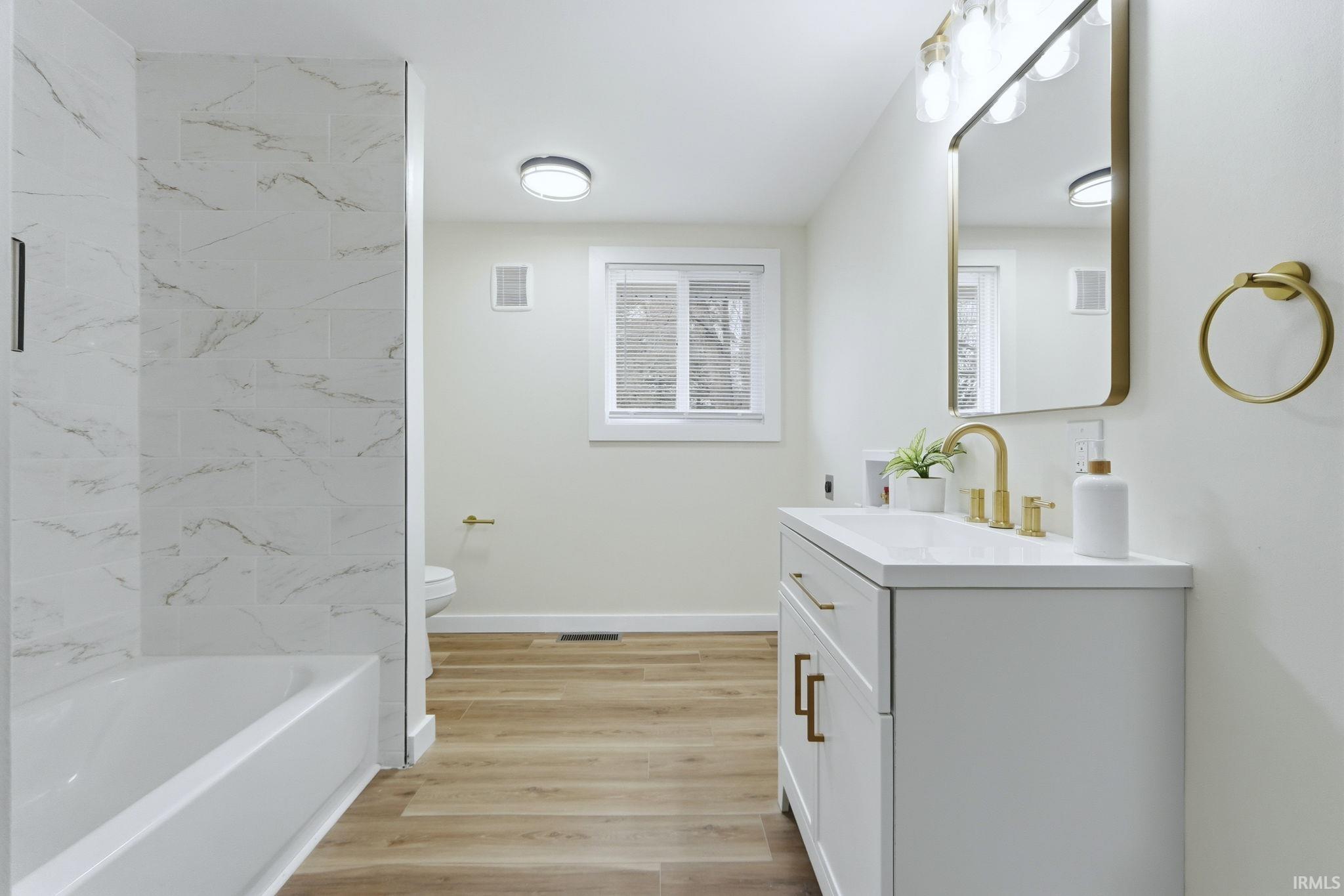 Full bath with vanity, light wood-style floors, and a combined bath / shower with marble appearance
