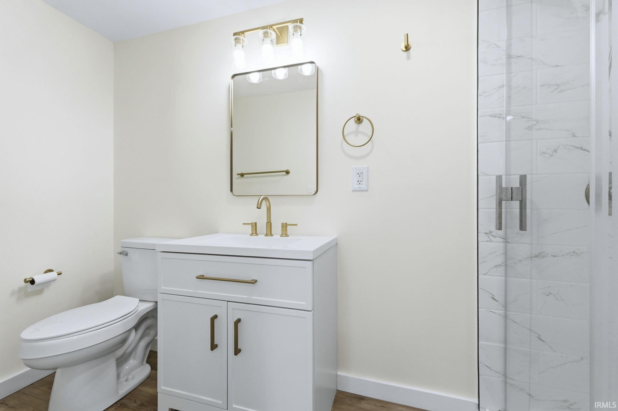 Bathroom featuring vanity, a marble finish shower, and dark wood-type flooring