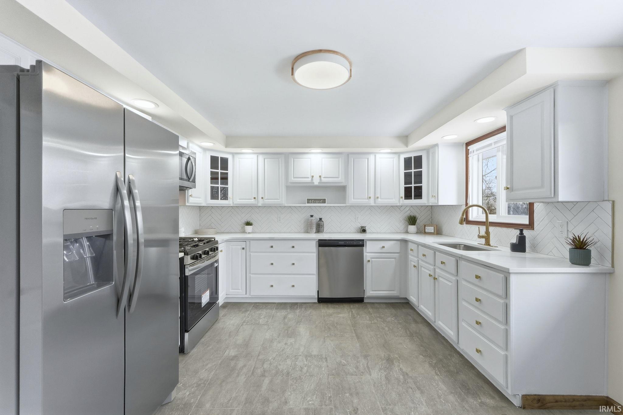 Kitchen featuring stainless steel appliances, glass insert cabinets, white cabinetry, and decorative backsplash