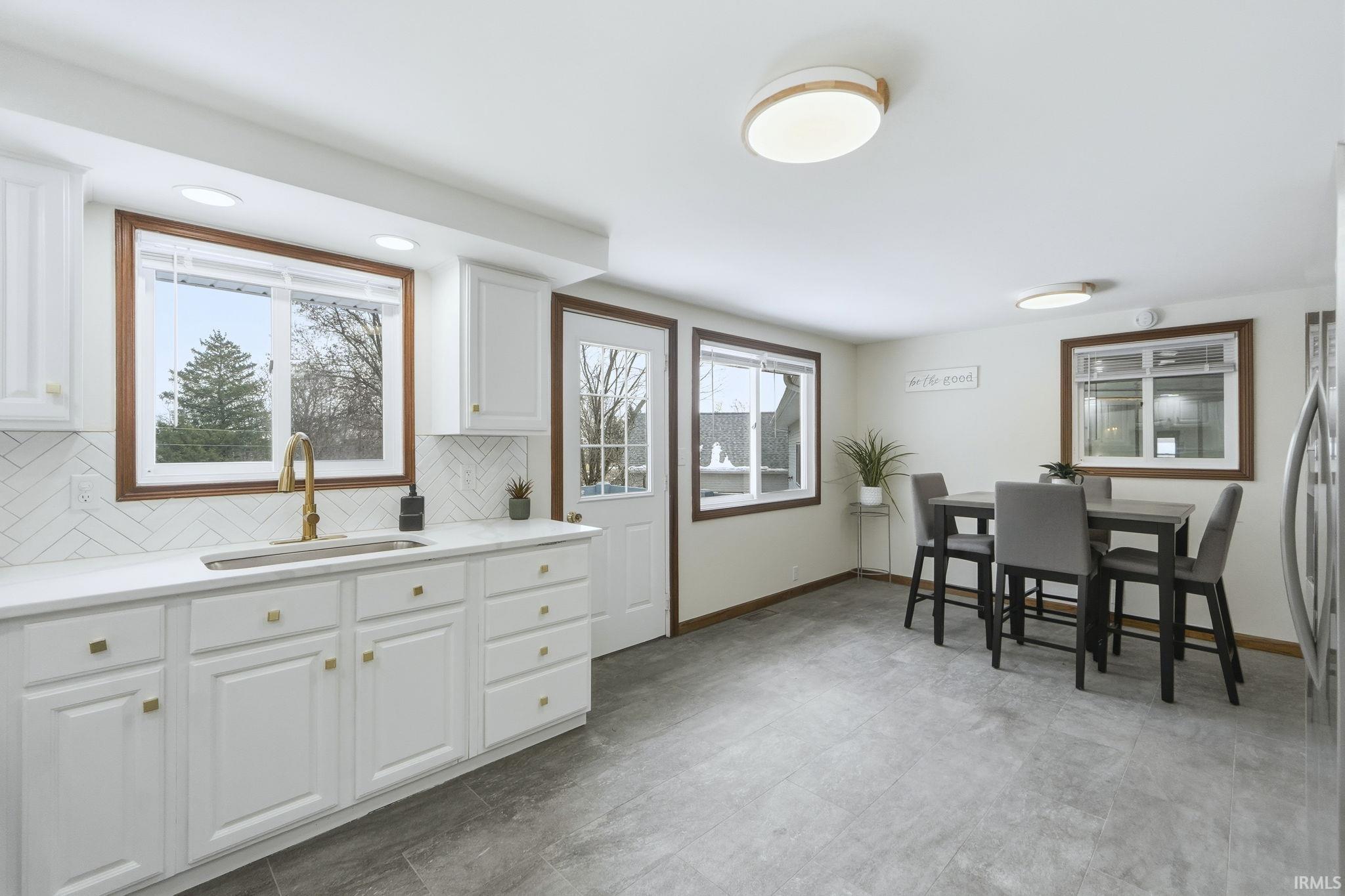 Kitchen featuring white cabinets, decorative backsplash, light stone counters, and freestanding refrigerator