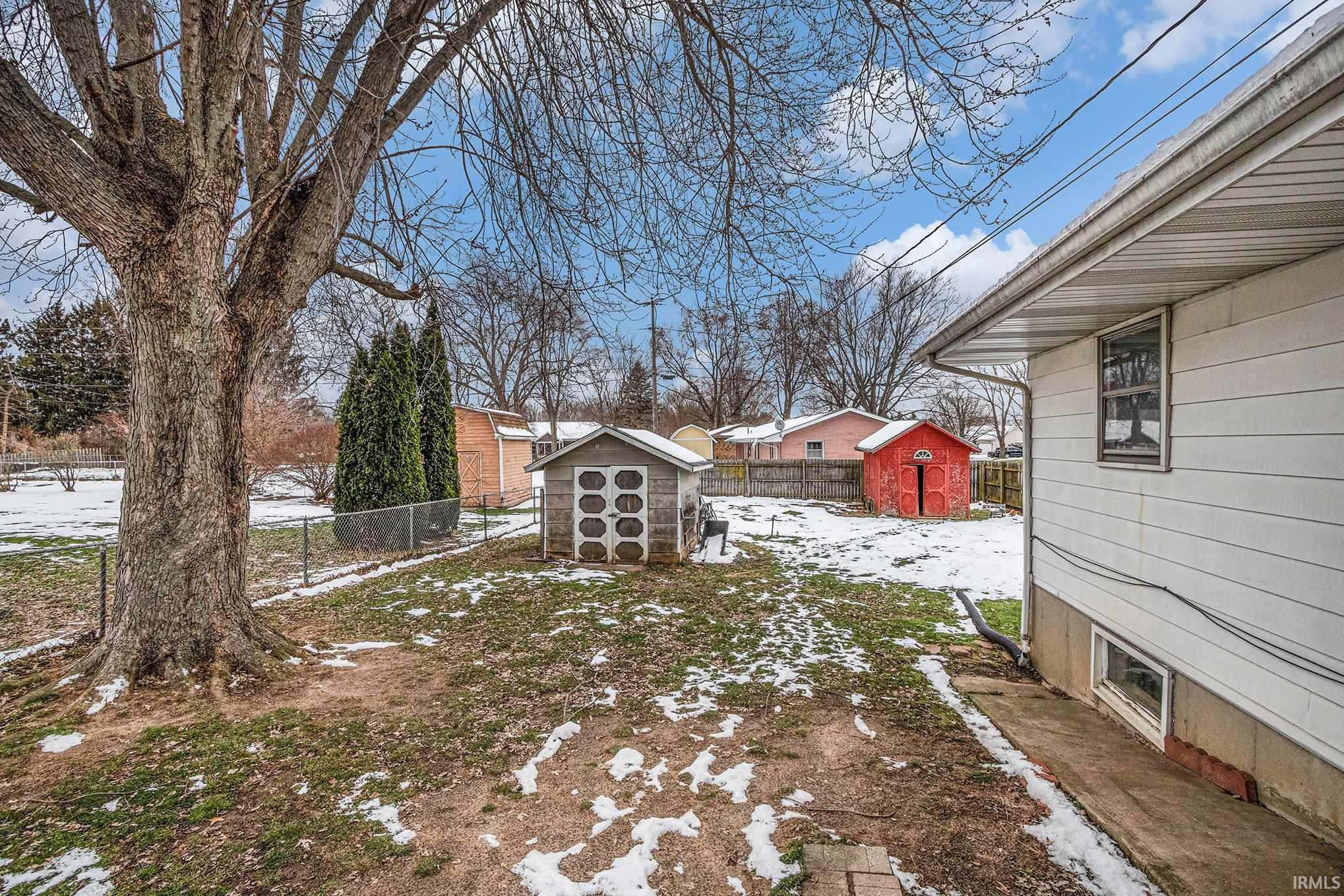 Yard layered in snow with a storage unit and a fenced backyard
